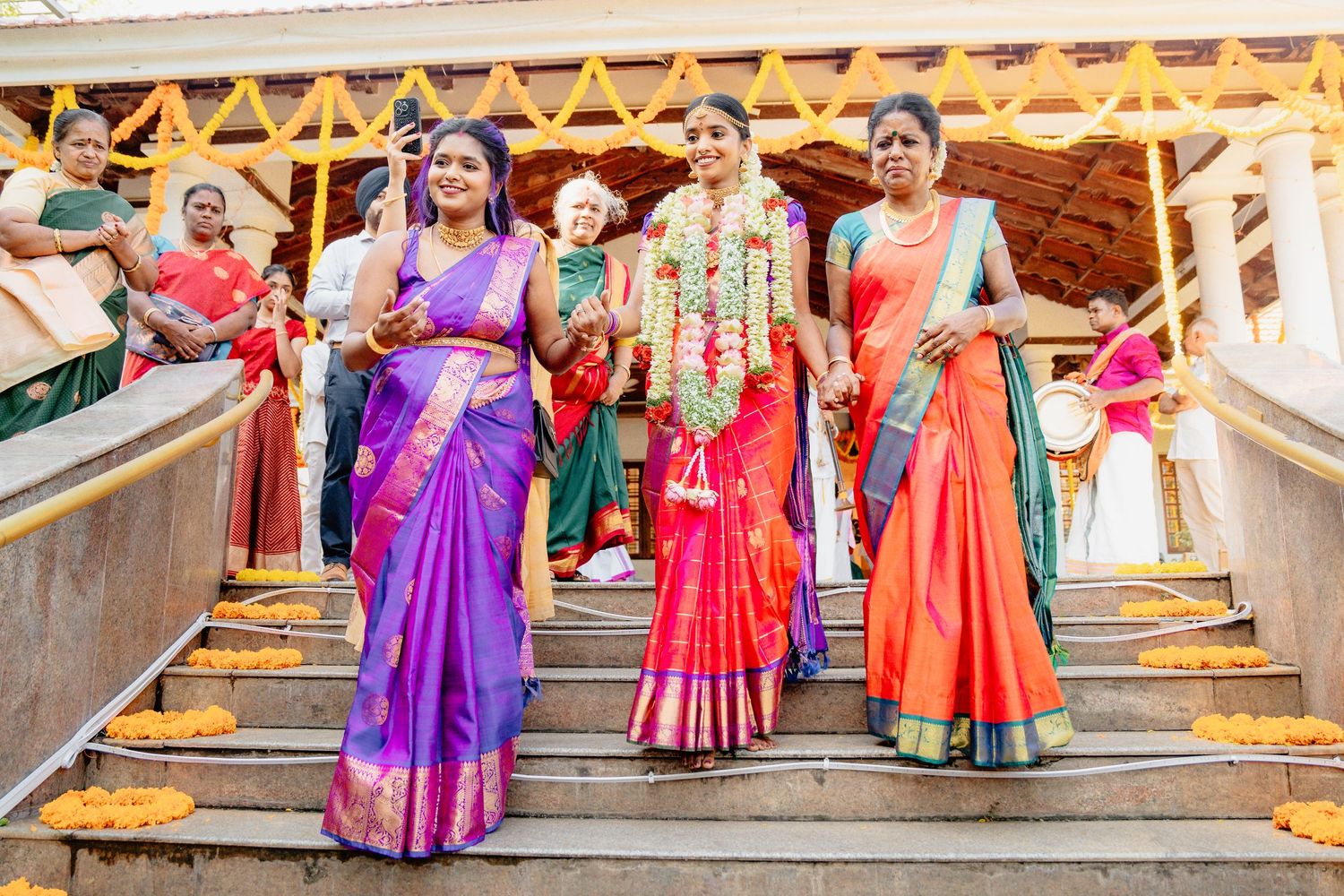 Guests in colorful traditional Indian sarees descend ornate stairs during a festive celebration.
