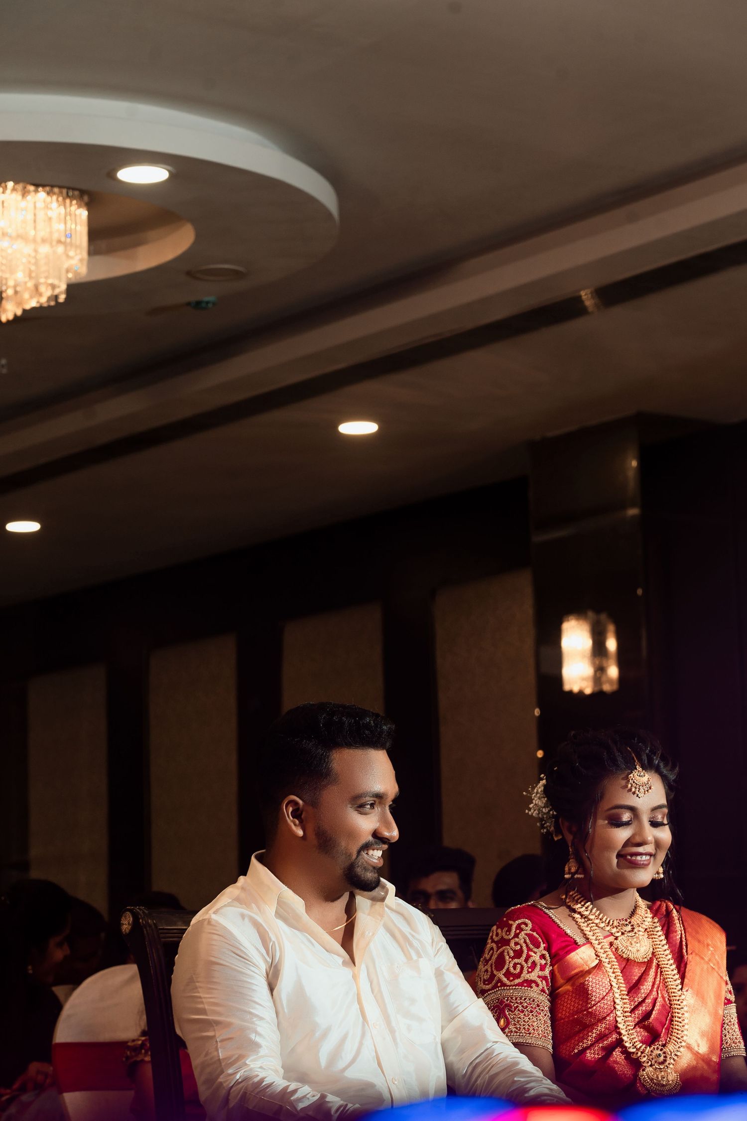 Wedding reception scene with traditional attire and elegant ceiling lighting.
