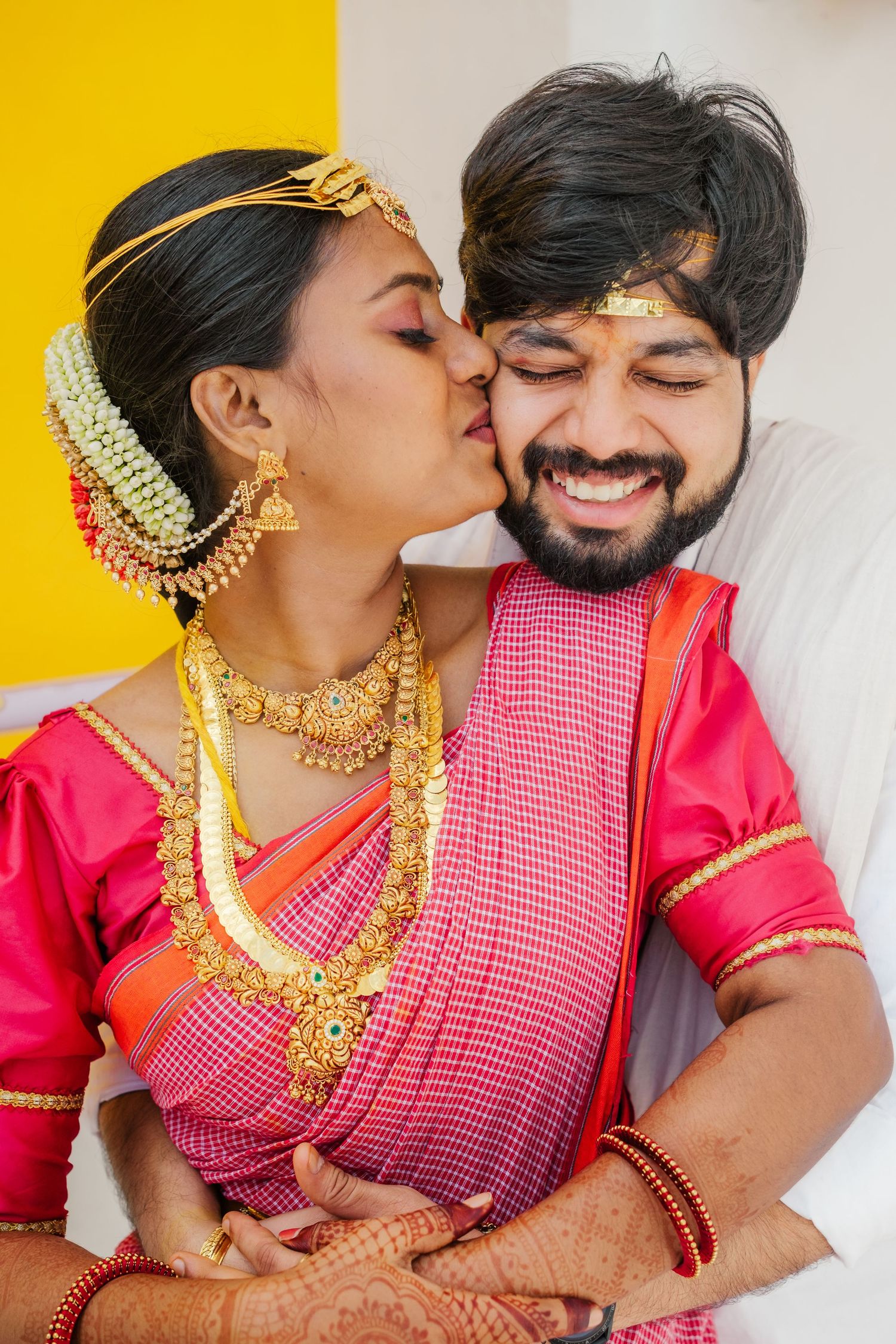 Traditional South Indian wedding portrait with bride in red silk saree and gold jewelry.
