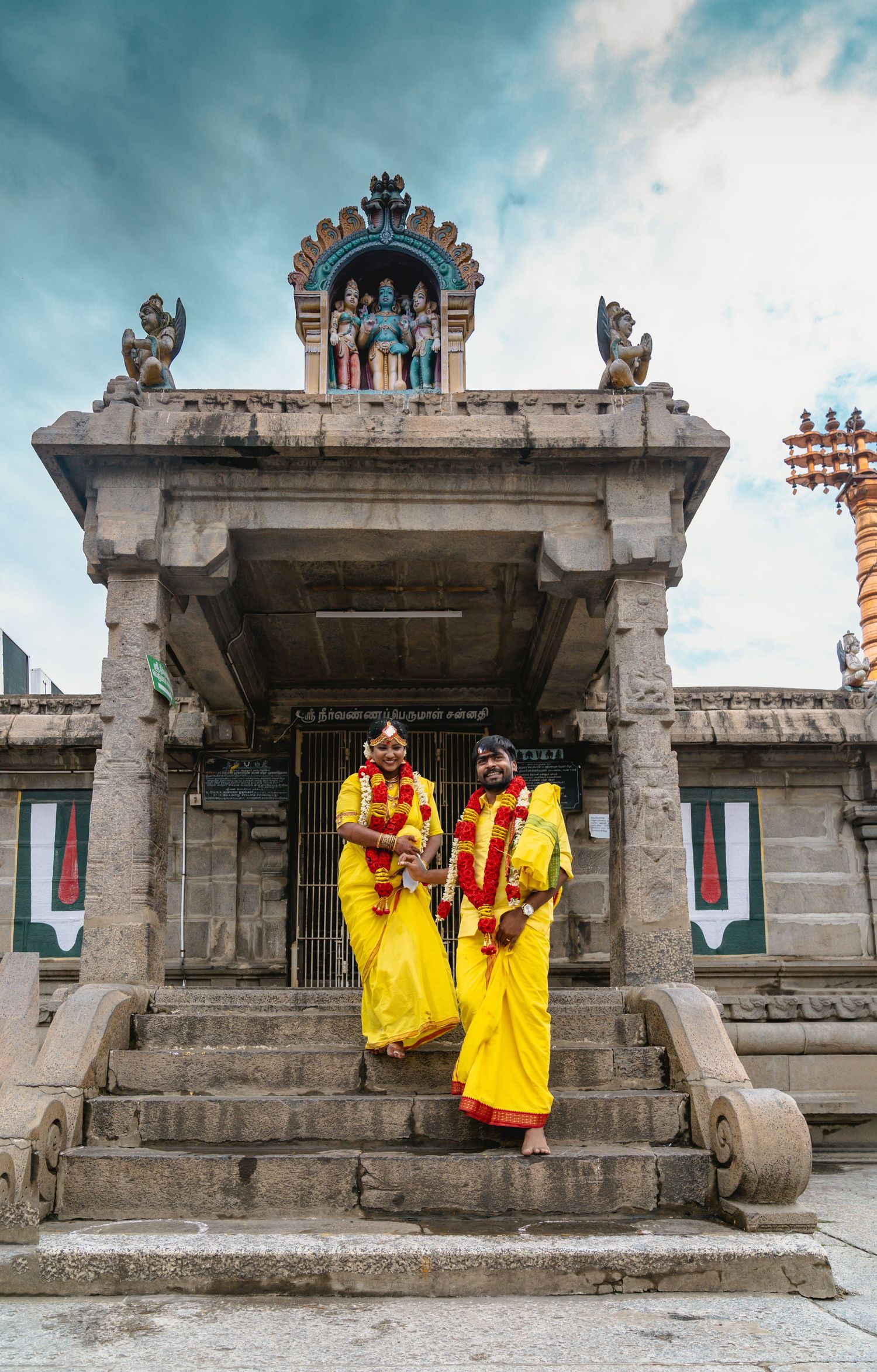Two figures in bright yellow saris pose elegantly on historic temple steps.
