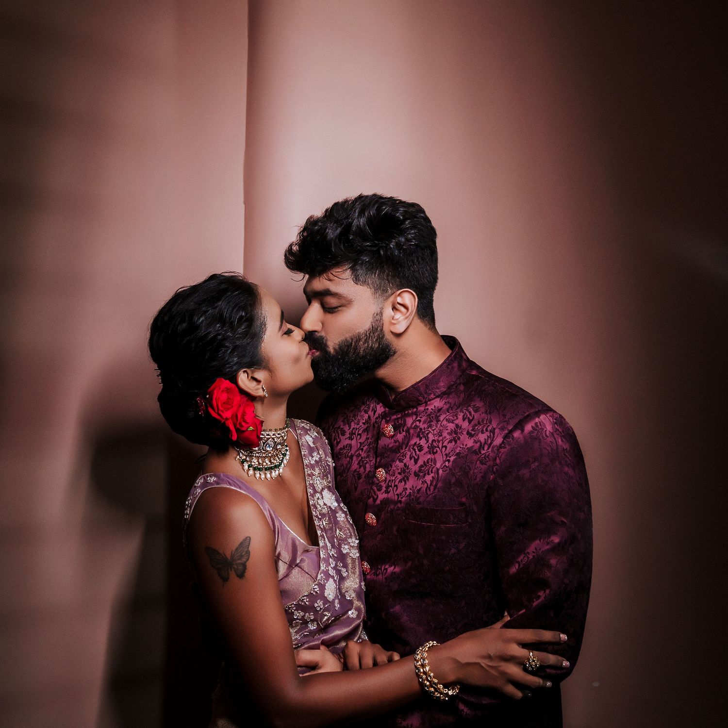Romantic couple in traditional Indian attire sharing an intimate moment against a burgundy backdrop.