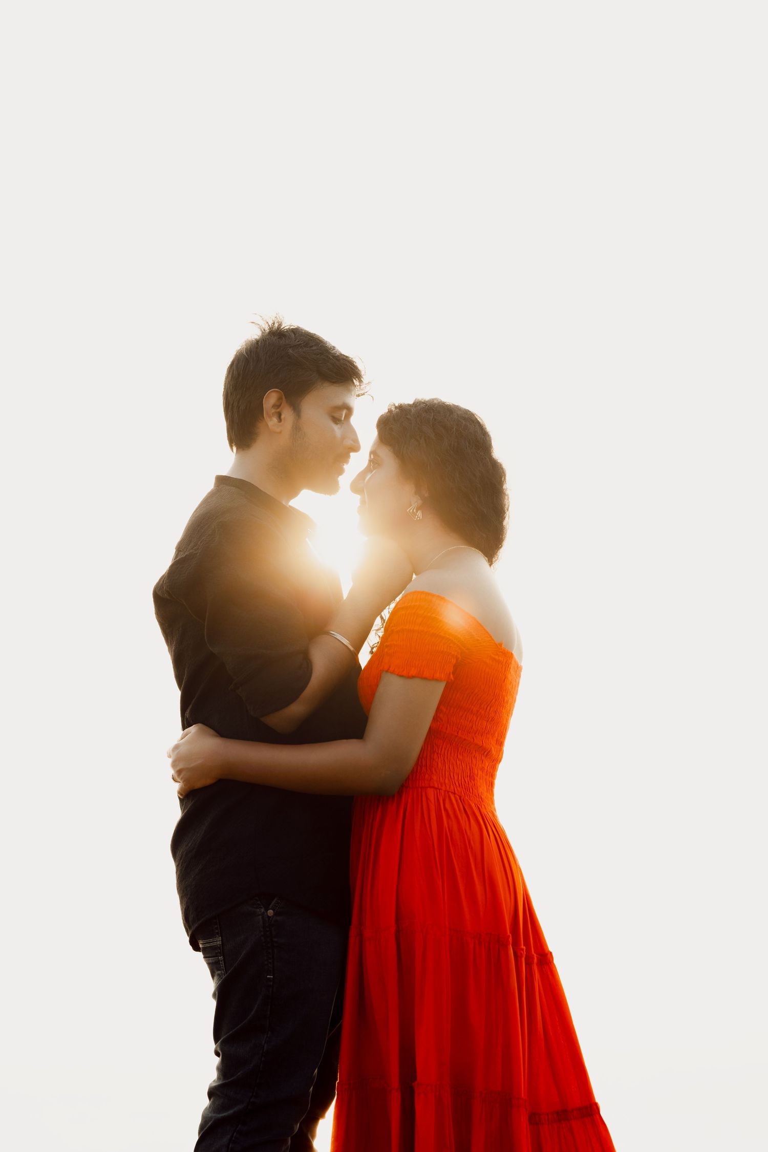 A silhouetted couple embraces against bright sunlight, with the woman wearing a vibrant red dress.