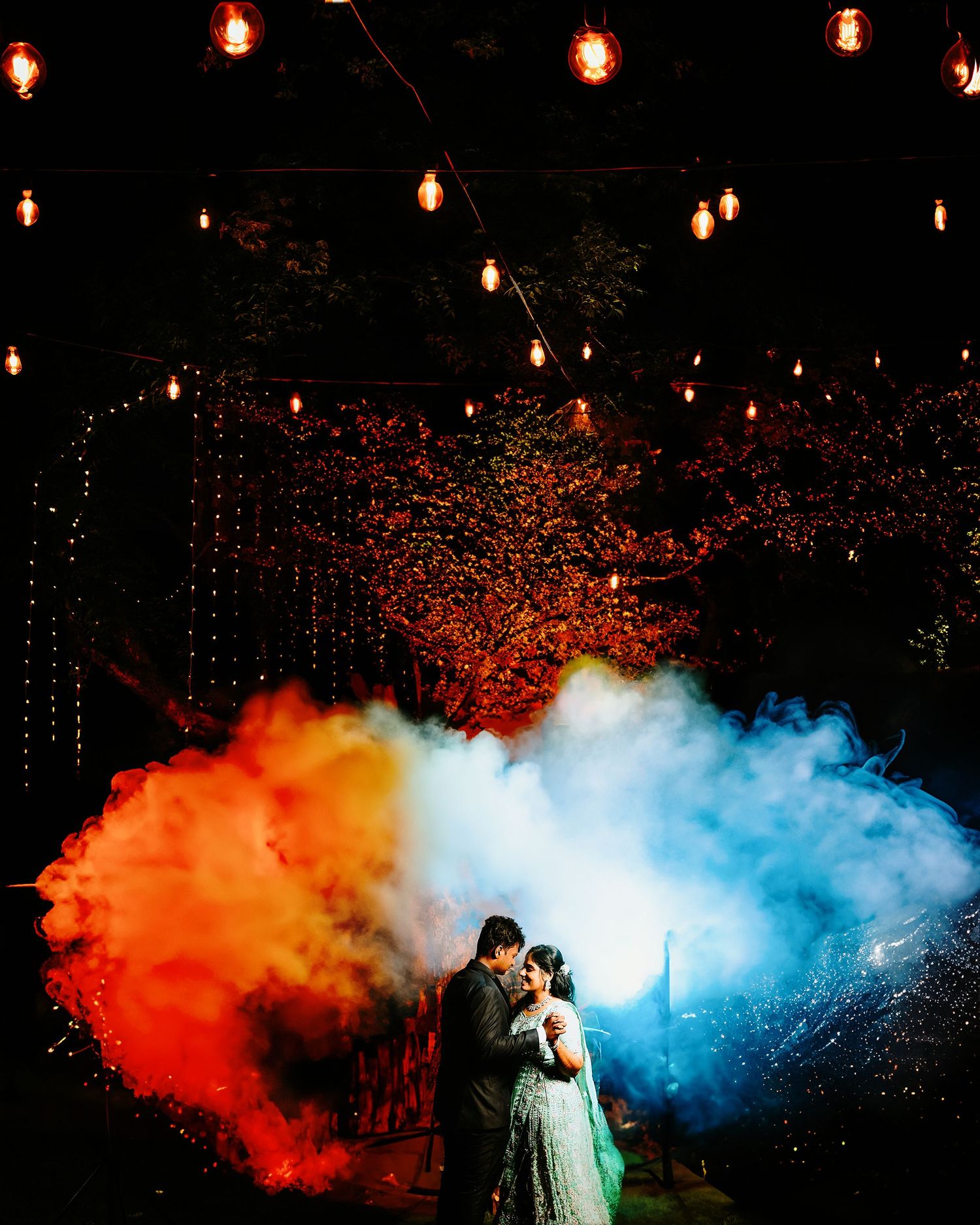 Magical moment captured with red and blue smoke effects creating contrast under warm string lighting.