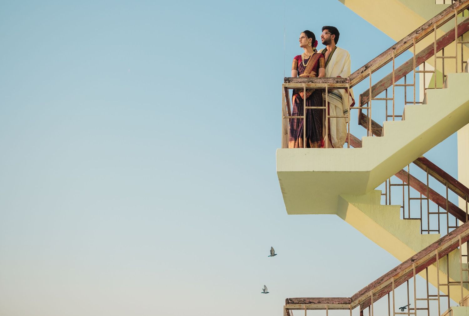 People climbing multiple parallel staircases in a geometric pattern against blue sky.