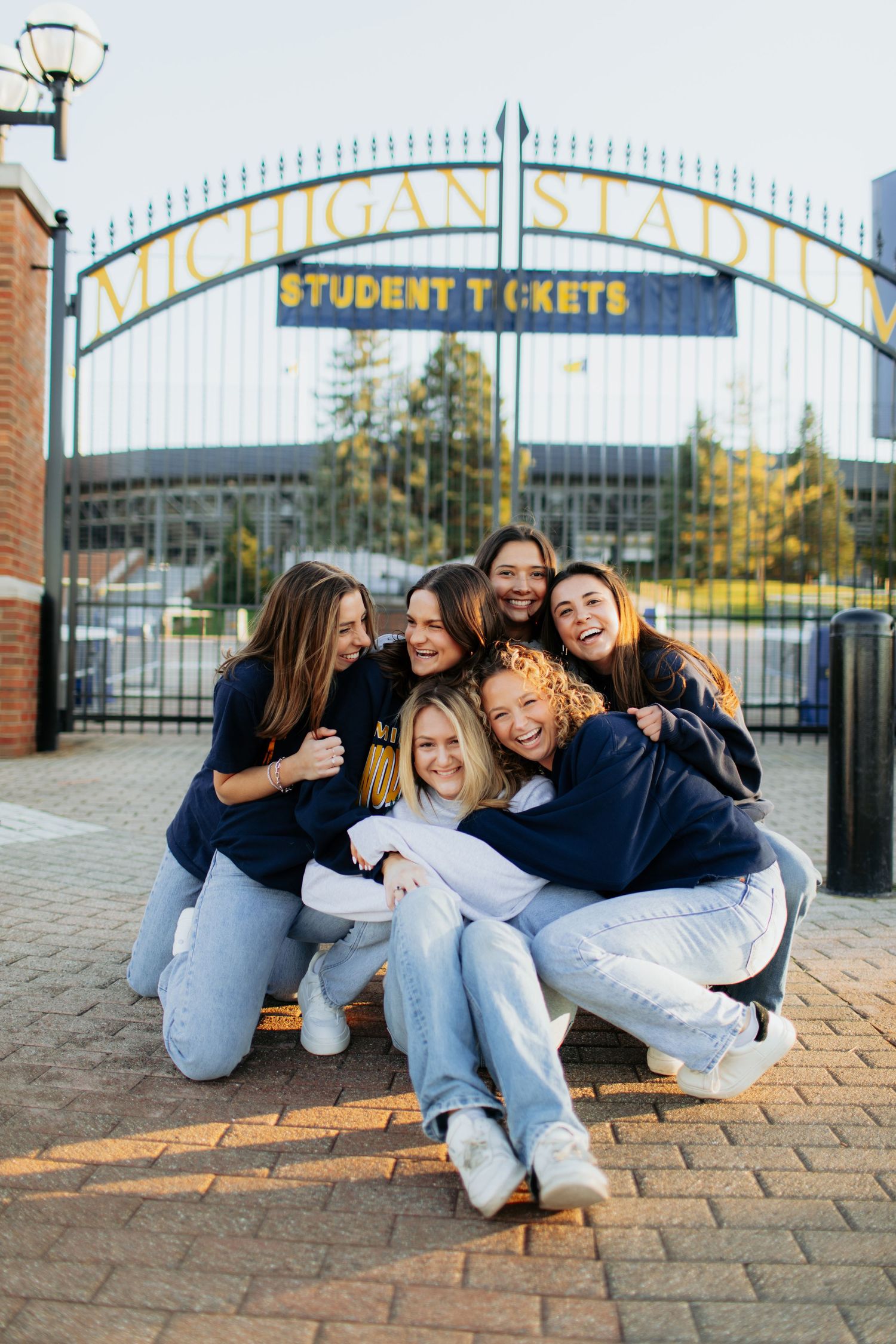 Group of friends hugging and laughing together outside Michigan Stadium entrance.