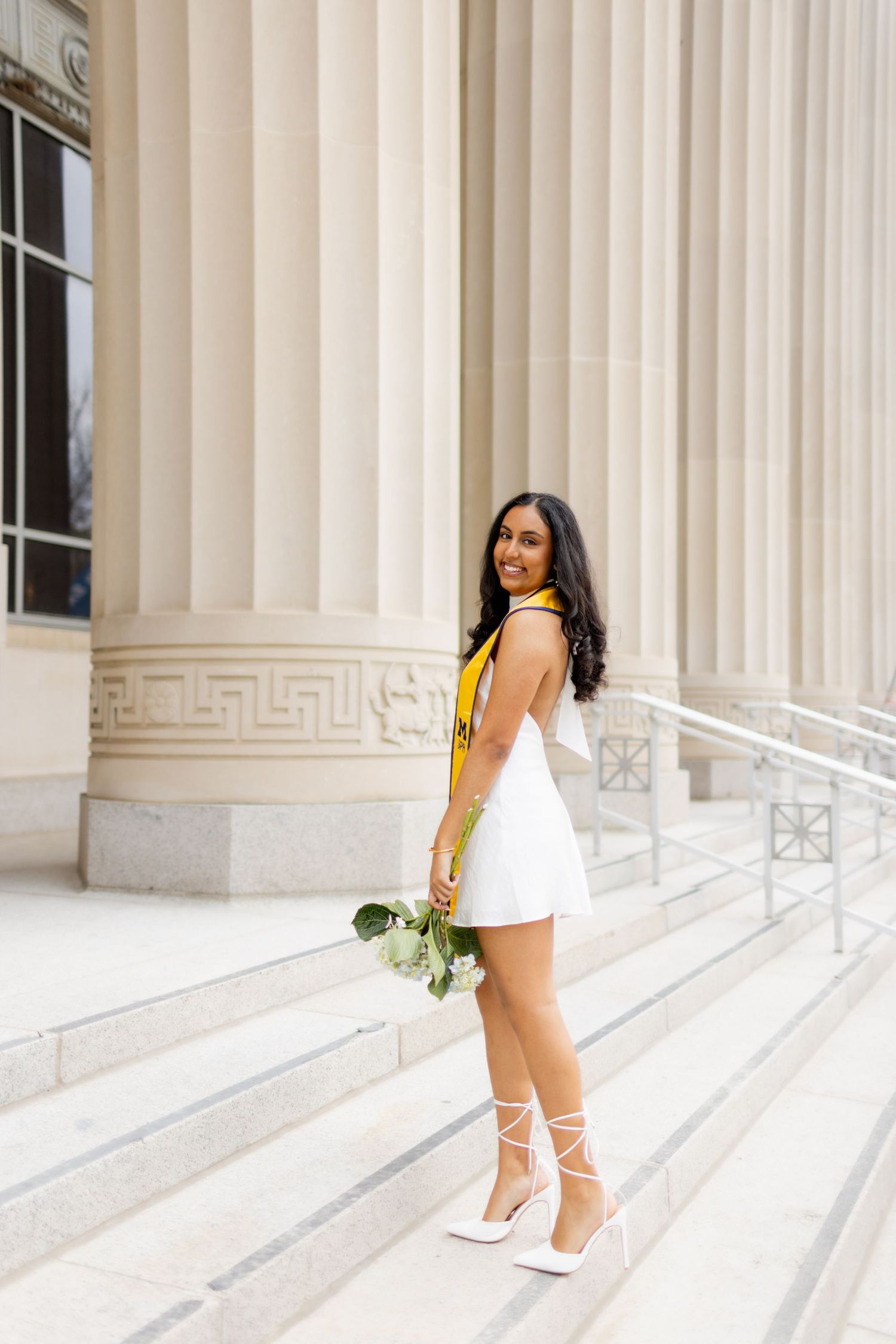 Bride in a white dress poses on grand marble steps with white columns in an elegant architectural setting.