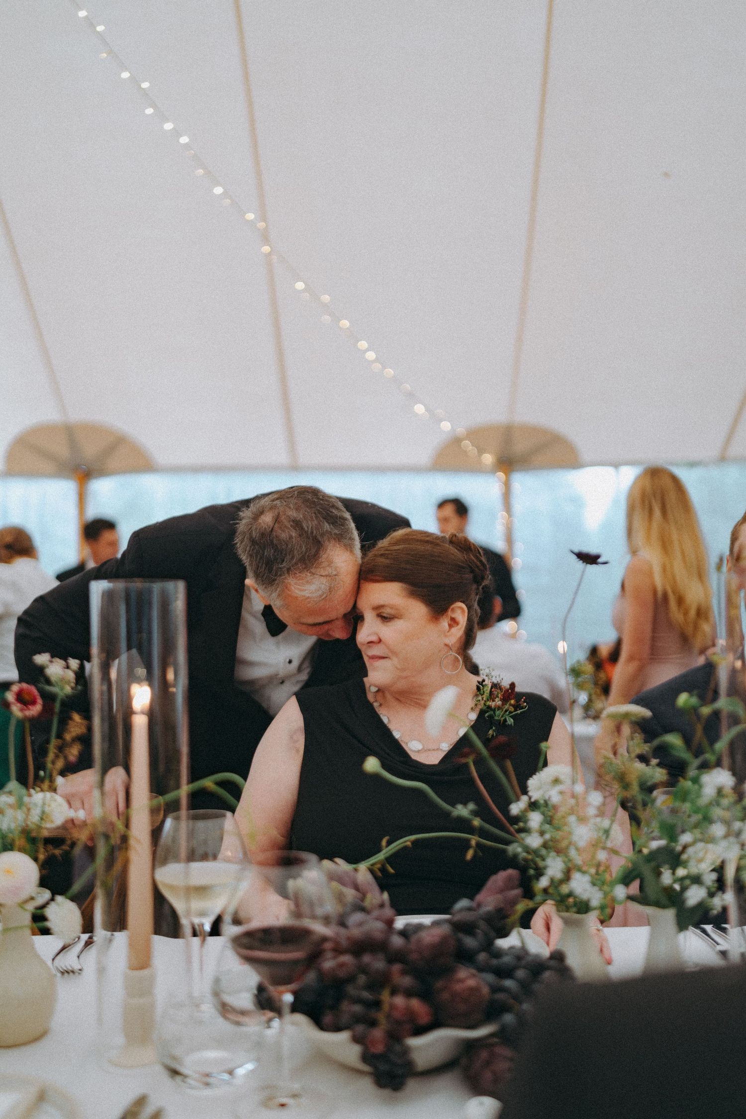 Candid moment of Senior couple sharing a quiet moment heads together at a table in a wedding reception tent