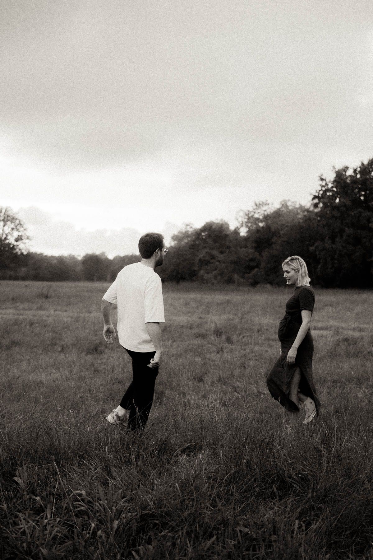 Black and white photo series shows people walking through a tall grass field under cloudy skies.