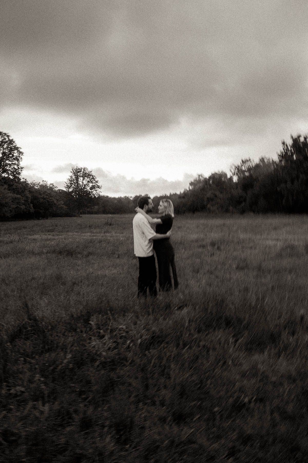 A black and white sequence of two people embracing in a misty field with dramatic cloudy skies overhead.