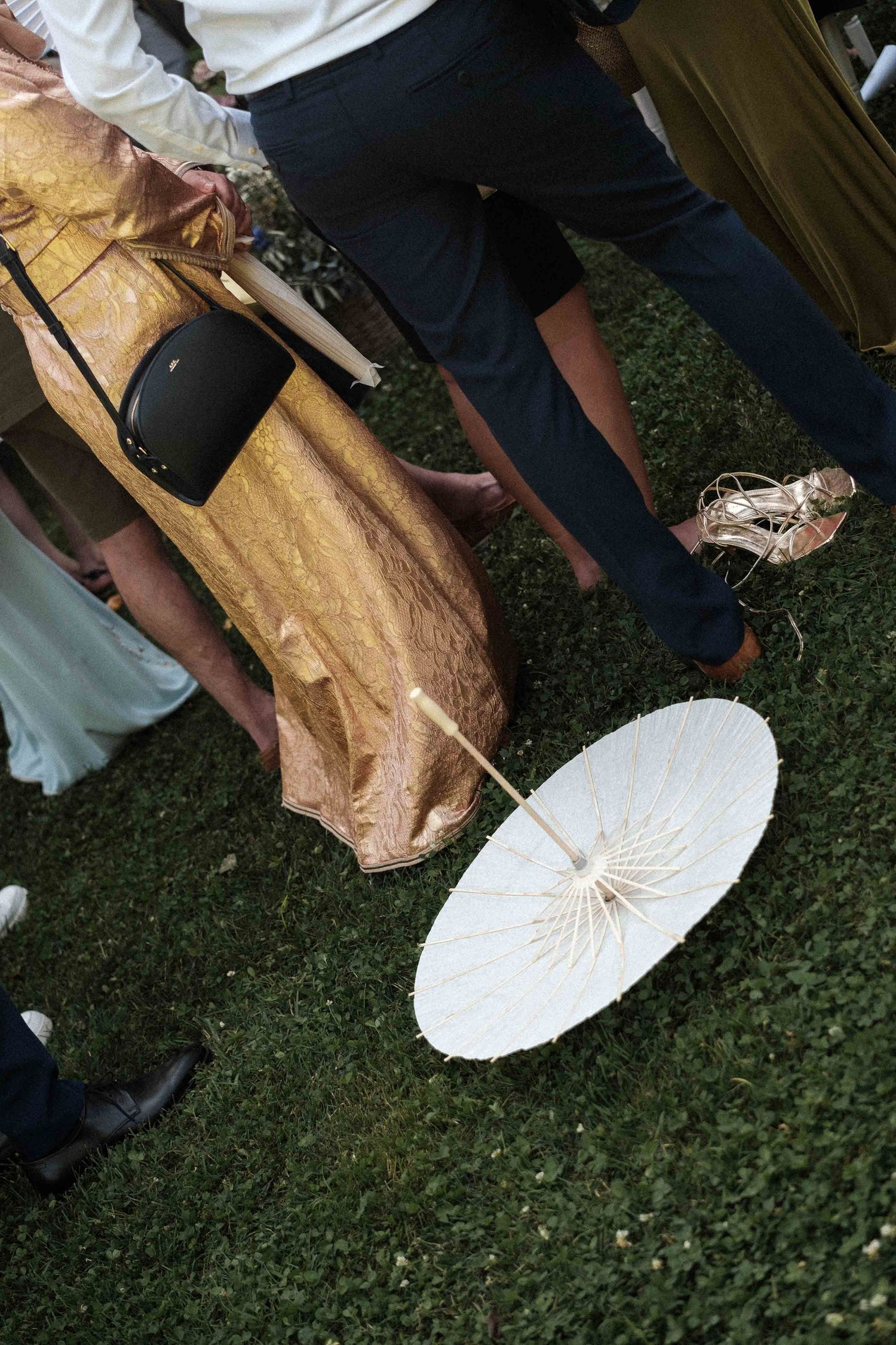 Wedding attendants holding decorative white paper parasols and wearing gold dresses at an outdoor event.
