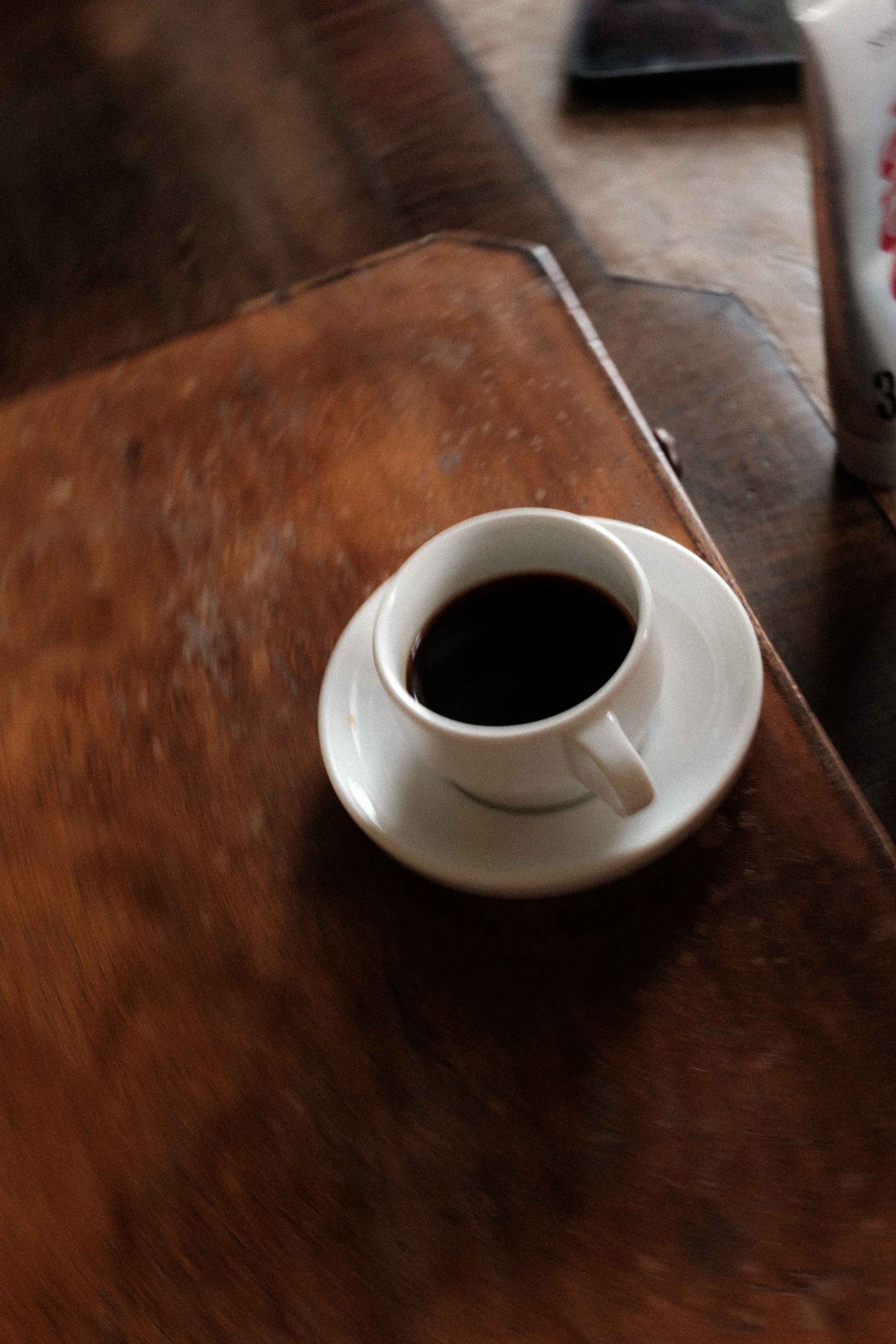 A white coffee cup filled with black coffee sits on a dark wooden table surface.