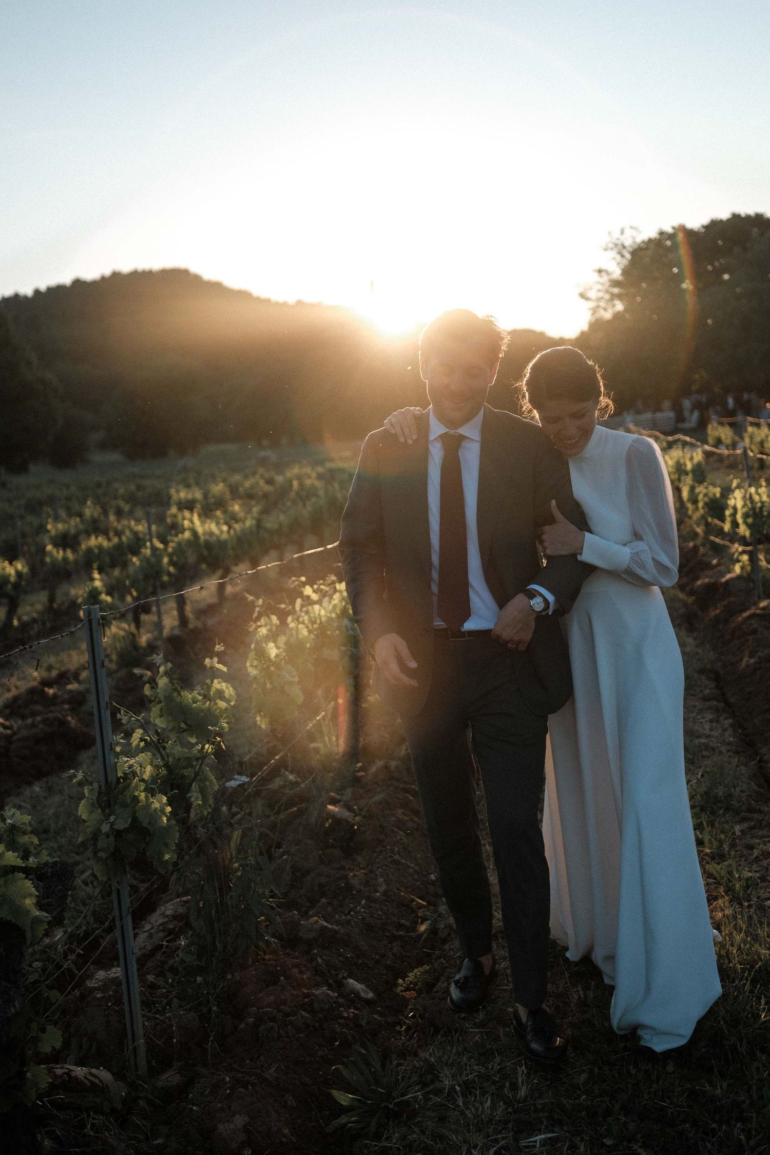 A couple embraces in silhouette against a golden sunset in a vineyard, creating a romantic backlit scene.