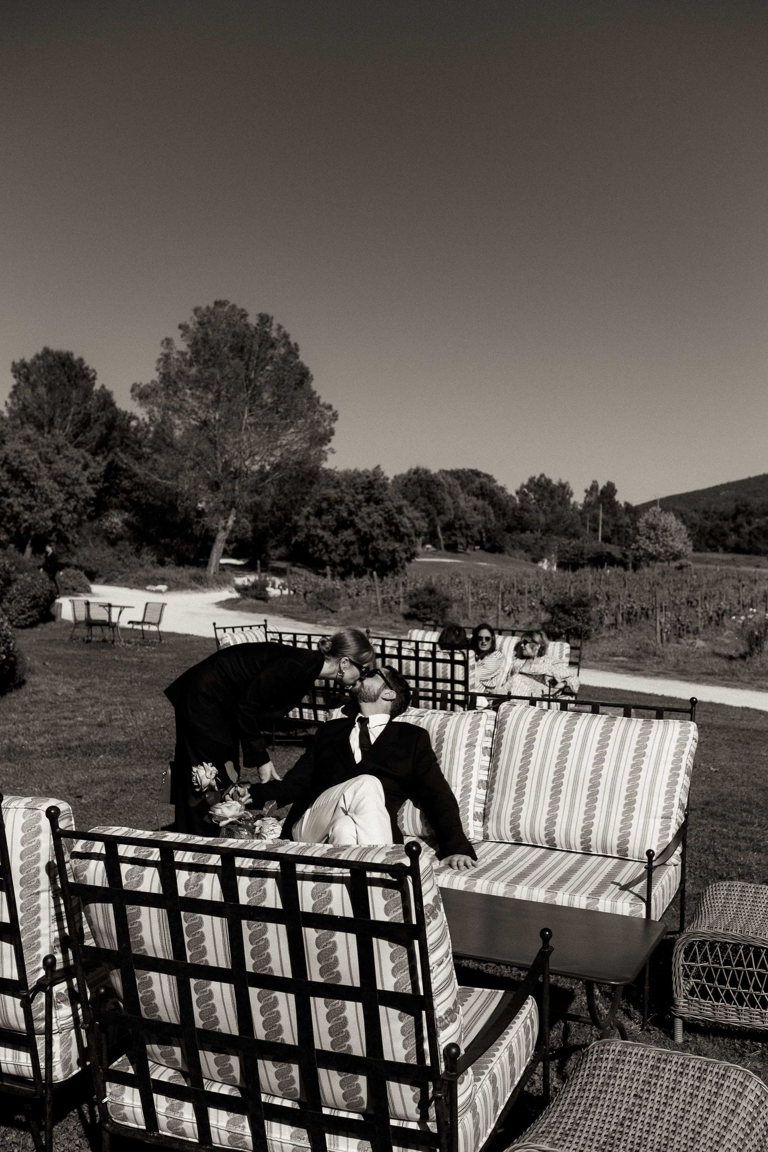 A black and white photo shows people seated on outdoor furniture in a garden setting.