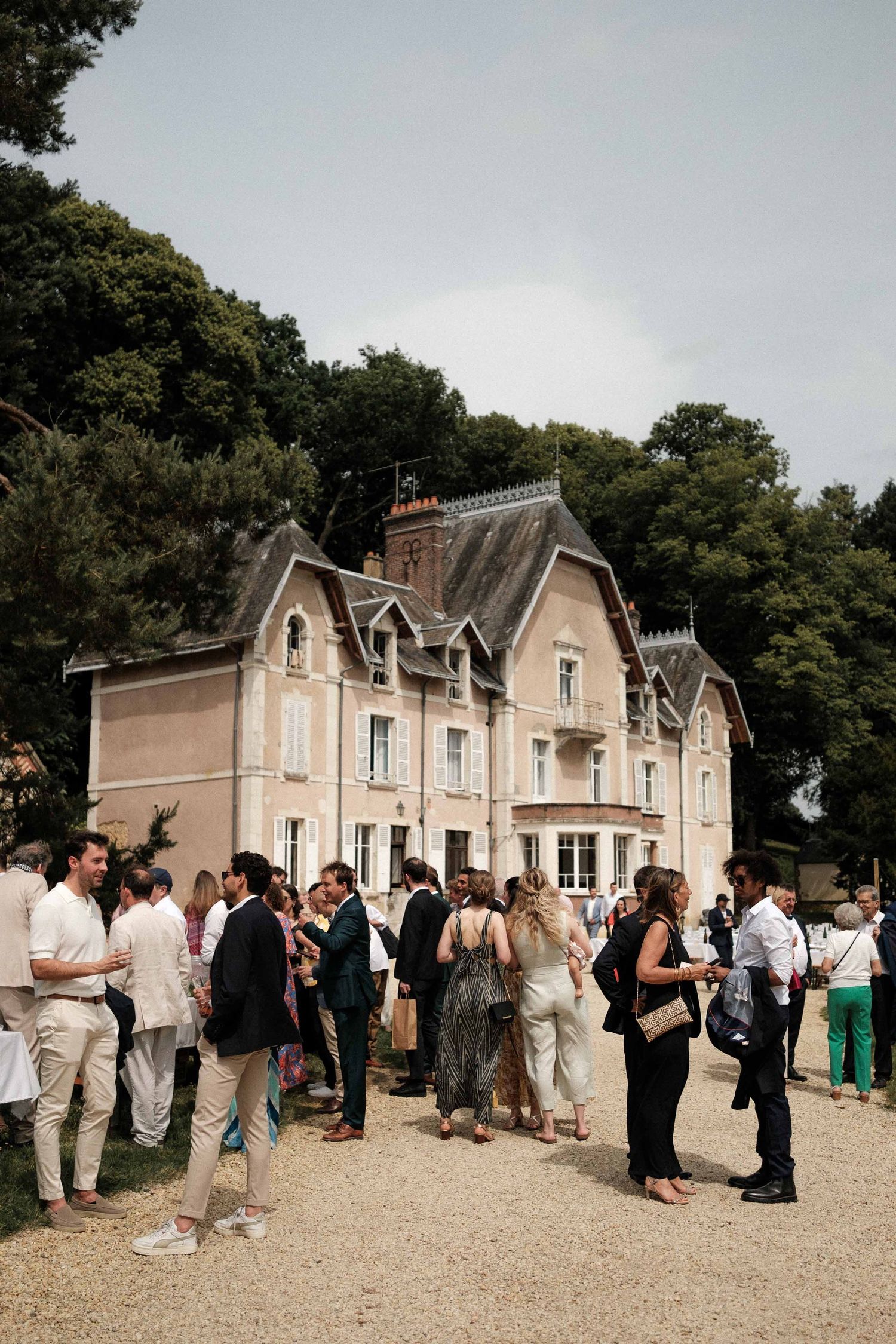 Wedding guests gather outside a beautiful Victorian-style manor house during an outdoor reception.