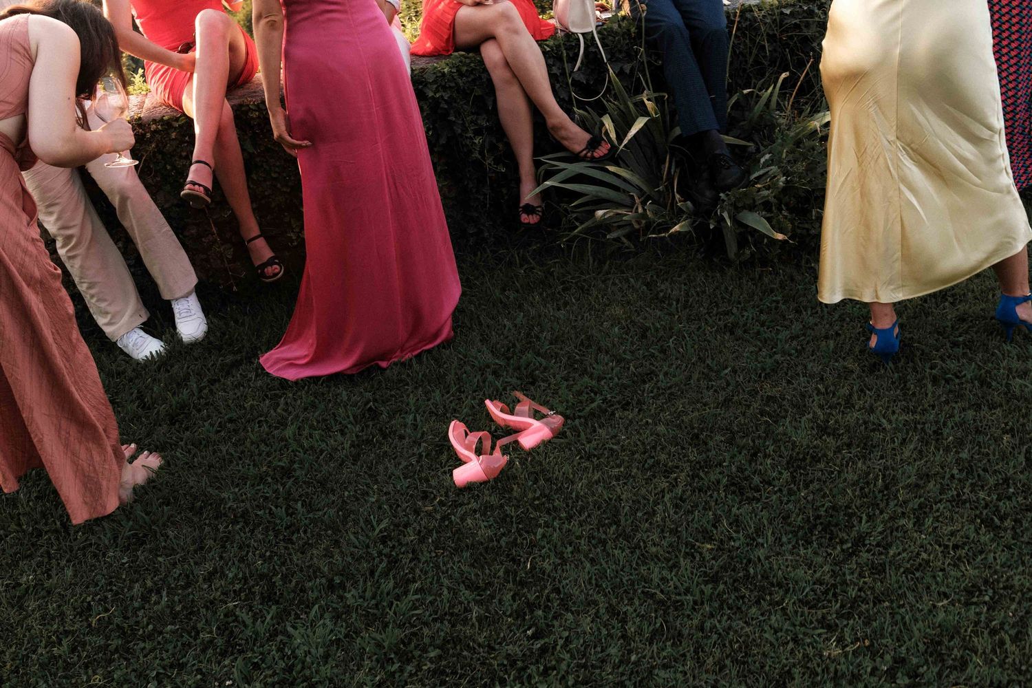 People in formal attire dance and celebrate on a grassy lawn at an outdoor party event.