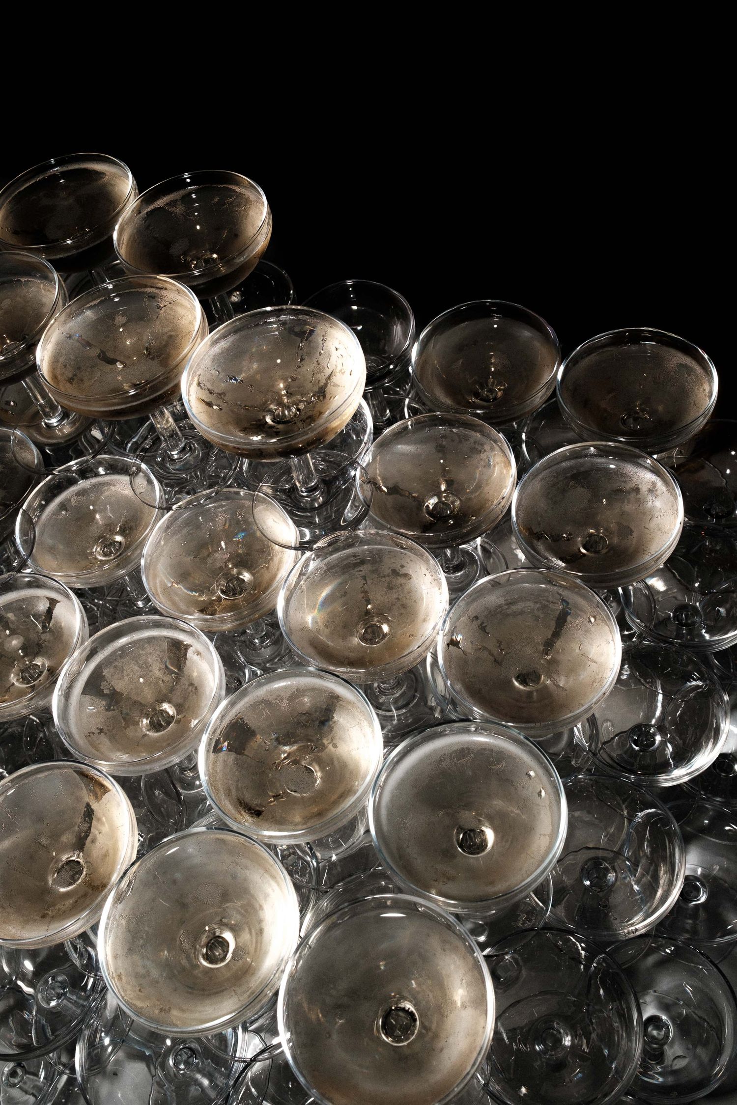 Multiple empty champagne coupes arranged in rows on a dark reflective surface create an elegant pattern.