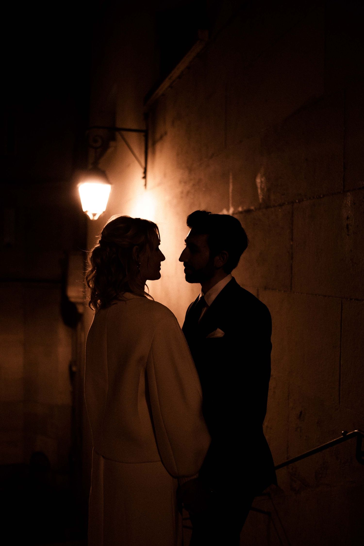 Silhouetted couple standing close together in romantic poses against warm glowing street lamps at night.