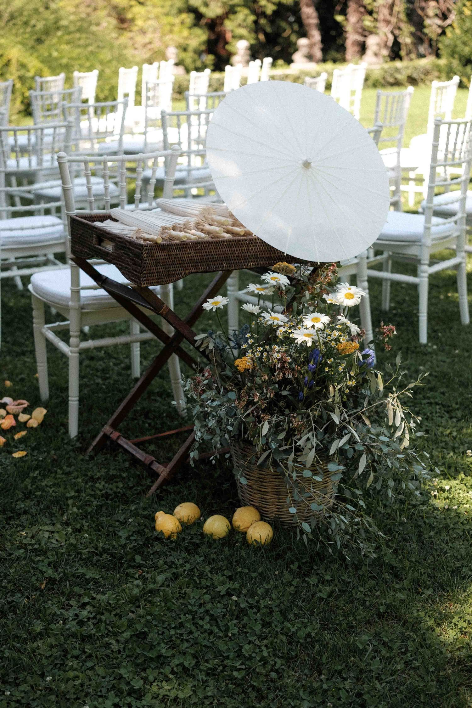 Wedding reception decor featuring rustic wooden tables with citrus fruits and white chairs on a grassy lawn.