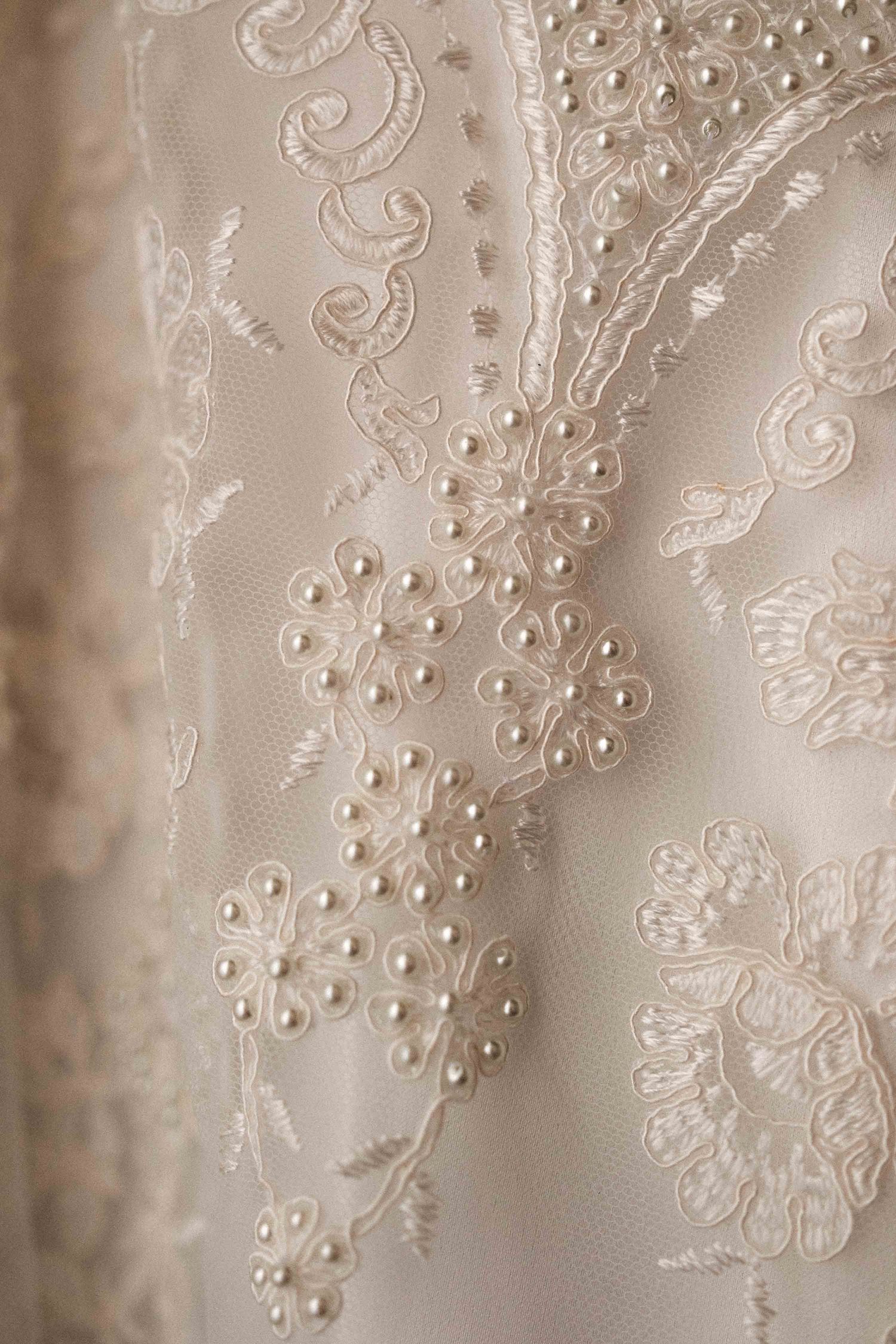 Delicate beaded lace fabric with floral embroidery and swirling patterns in ivory white.