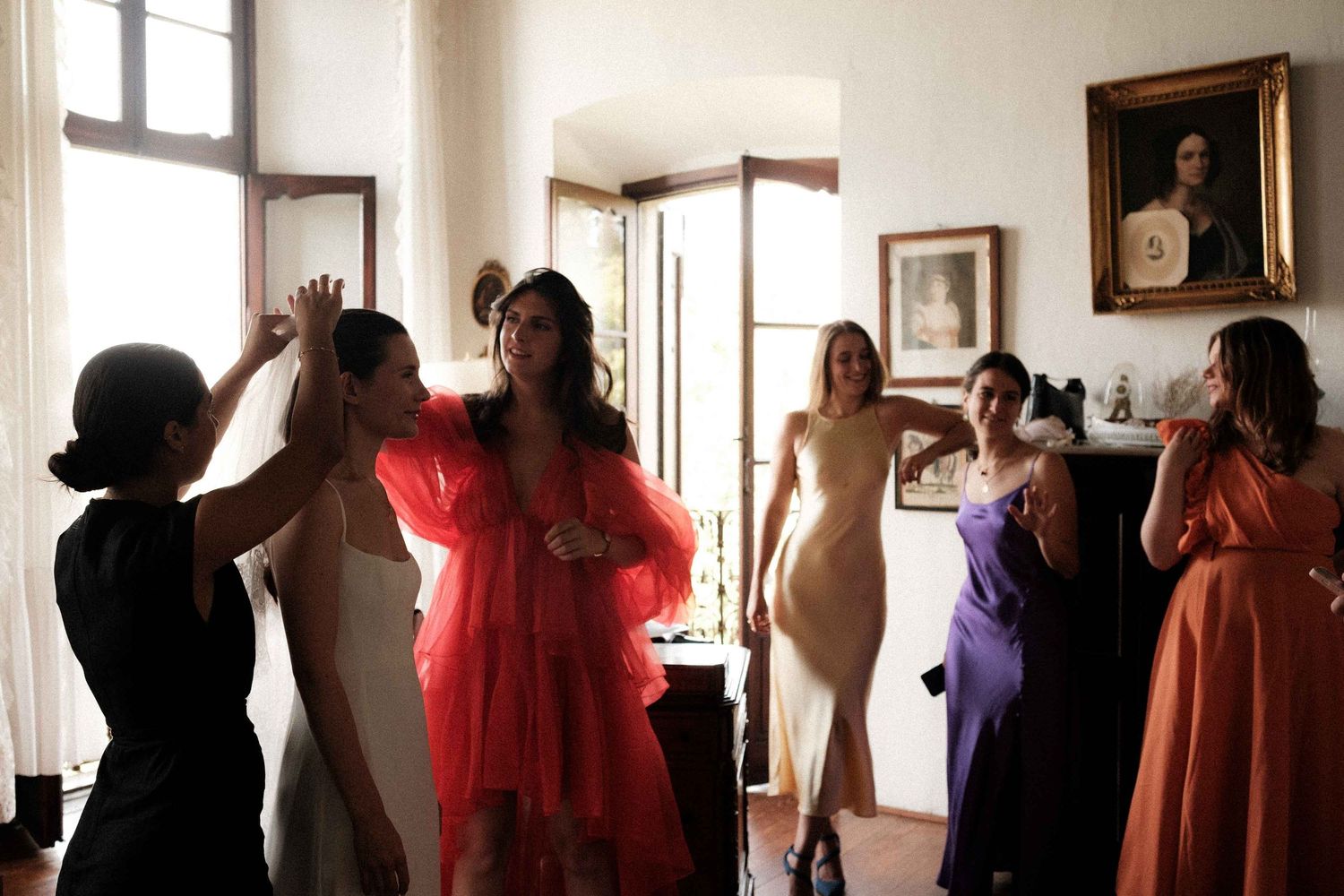 A series of silhouetted figures in colorful dresses dance and move in front of sunlit windows in an art gallery space.