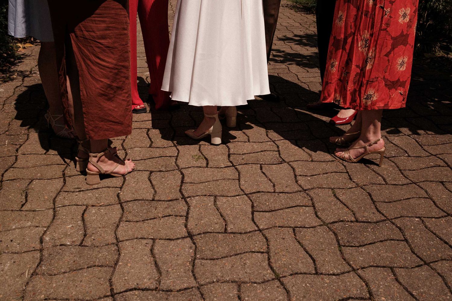 A group of people wearing red and white dresses walk along a cobblestone path during an outdoor gathering.