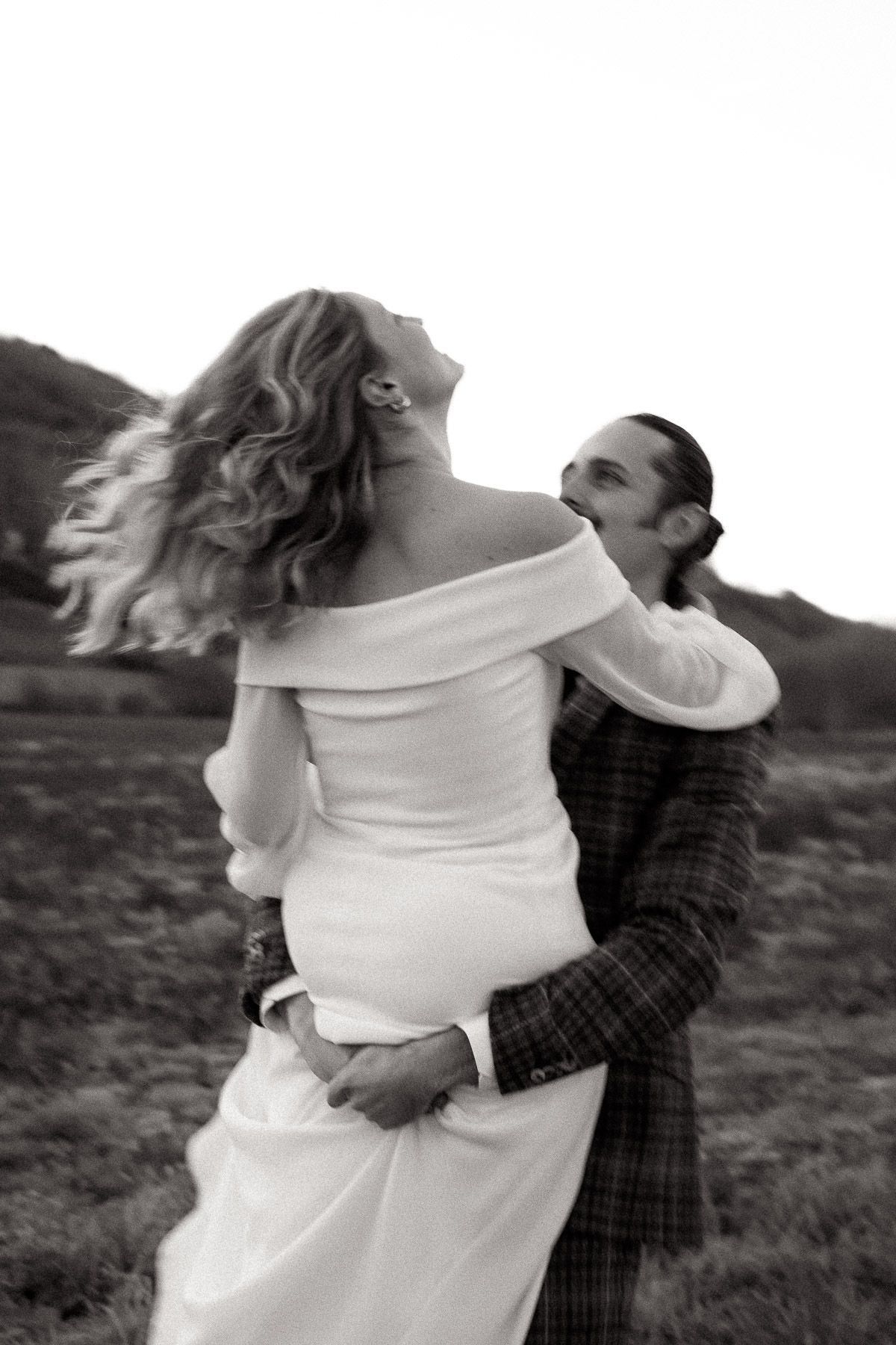 A couple embraces in a romantic black and white photo series showing intimate moments outdoors.
