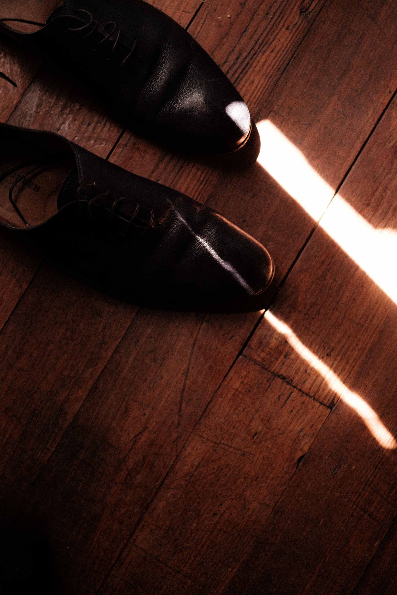 A series of shadows and light beams falling across wooden floorboards with a partial shoe visible in frame.