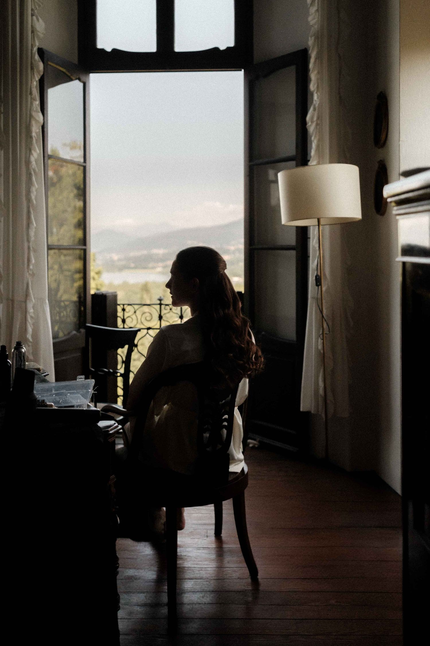 A dark silhouette sits in a room with large windows and natural light streaming in, creating a moody atmosphere.