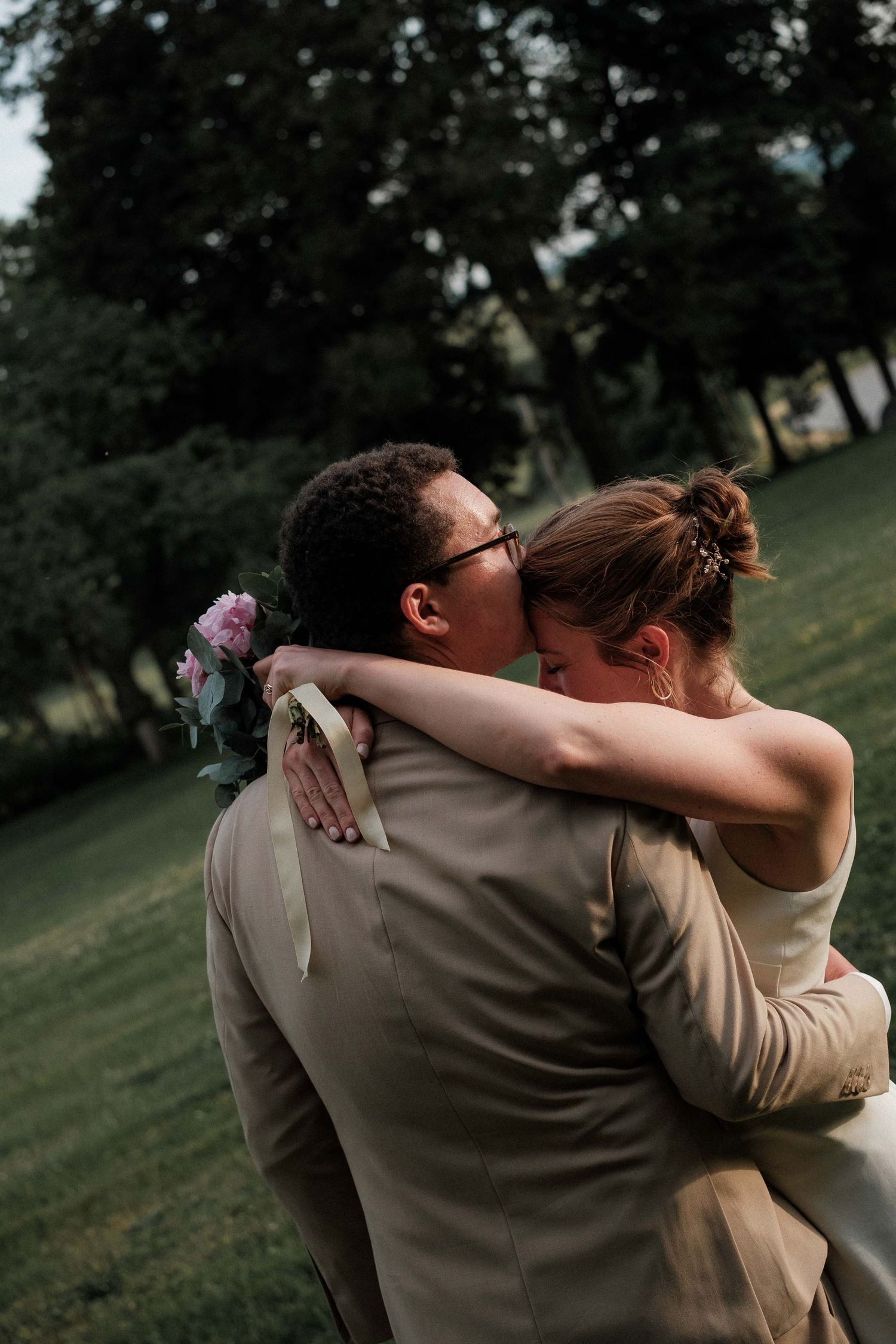 A tender embrace between two people in formal attire against a natural outdoor setting.