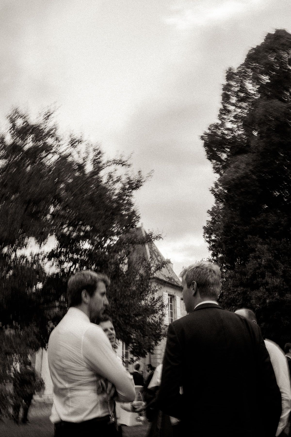 A black and white photo sequence showing people walking in a garden or park setting with trees in the background.