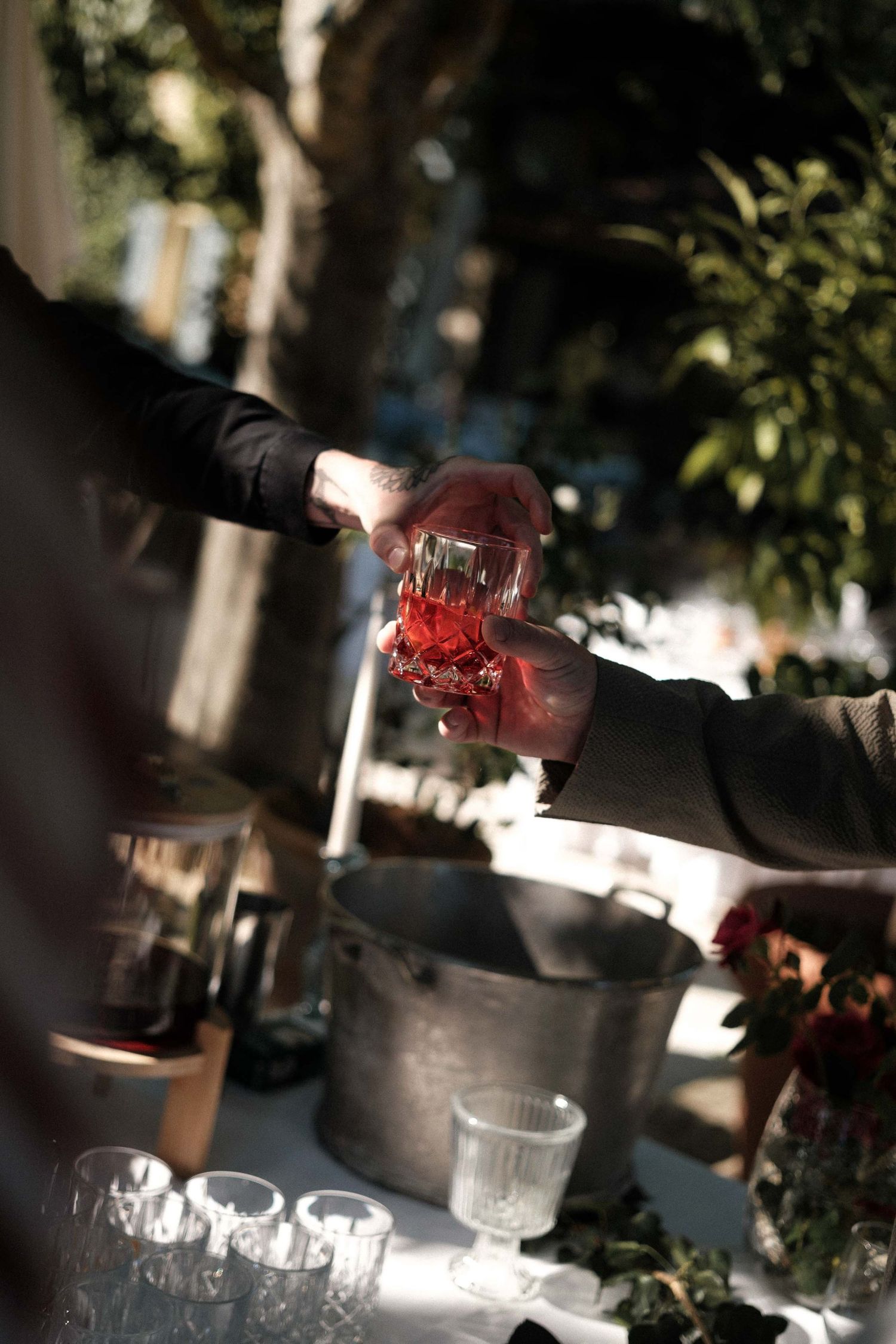 Wine glasses being filled with red wine in an outdoor setting with dappled sunlight.