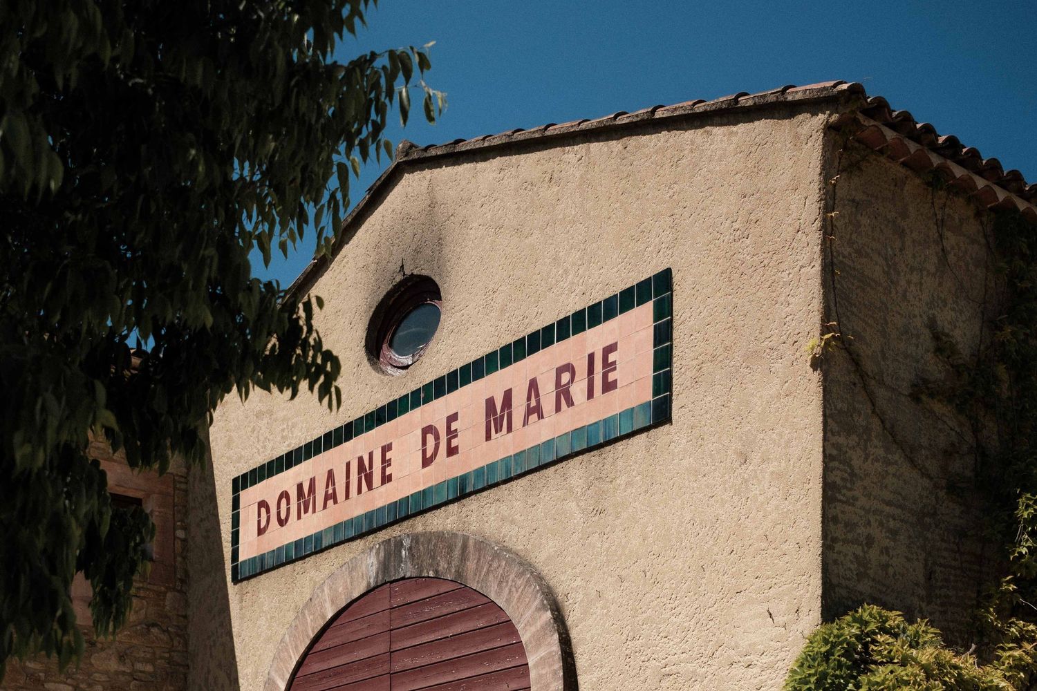 Rustic French winery building with 'Domaine de Mara' sign against a clear blue sky.
