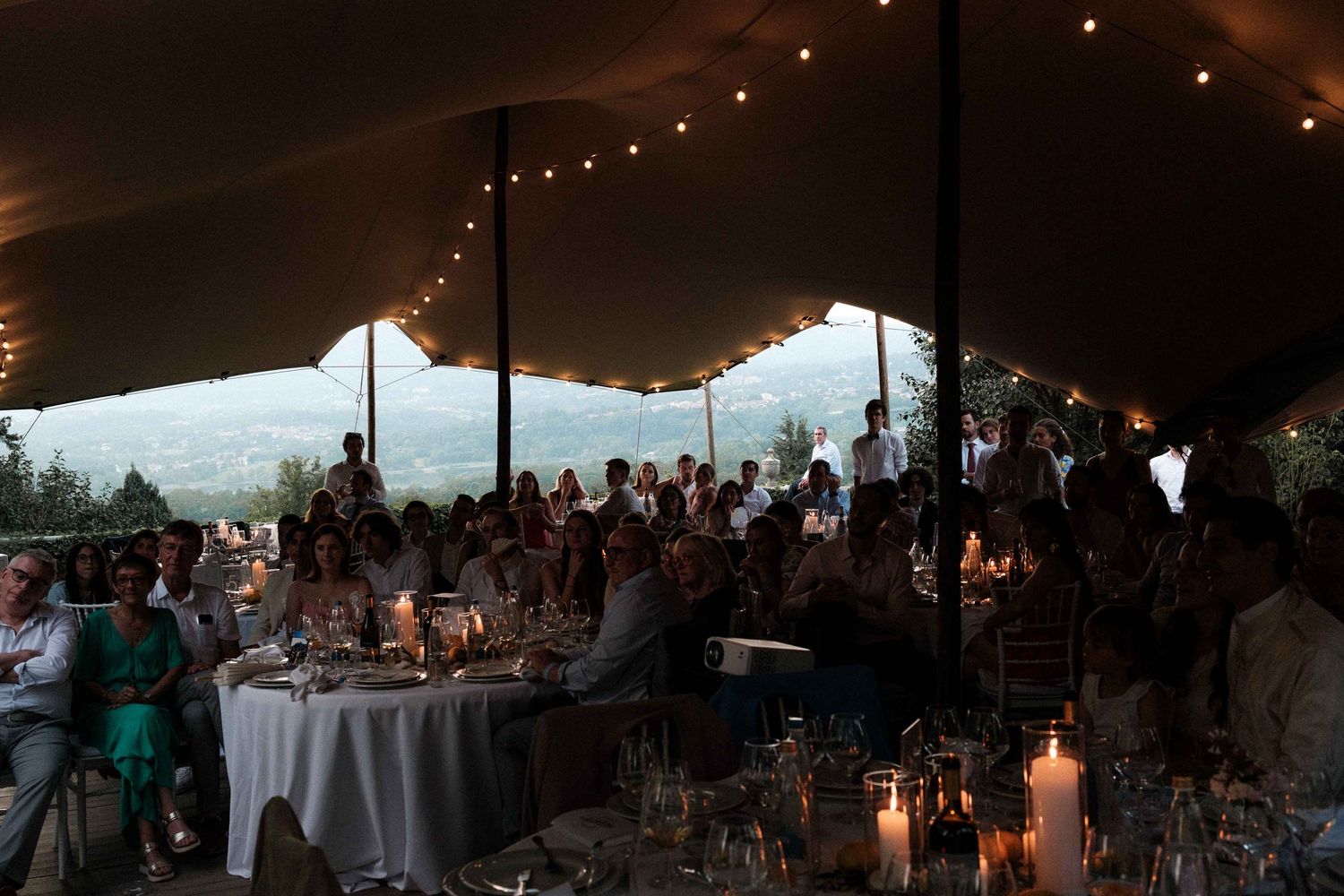Illuminated wedding reception tent at dusk with string lights creating a warm, romantic atmosphere for guests.