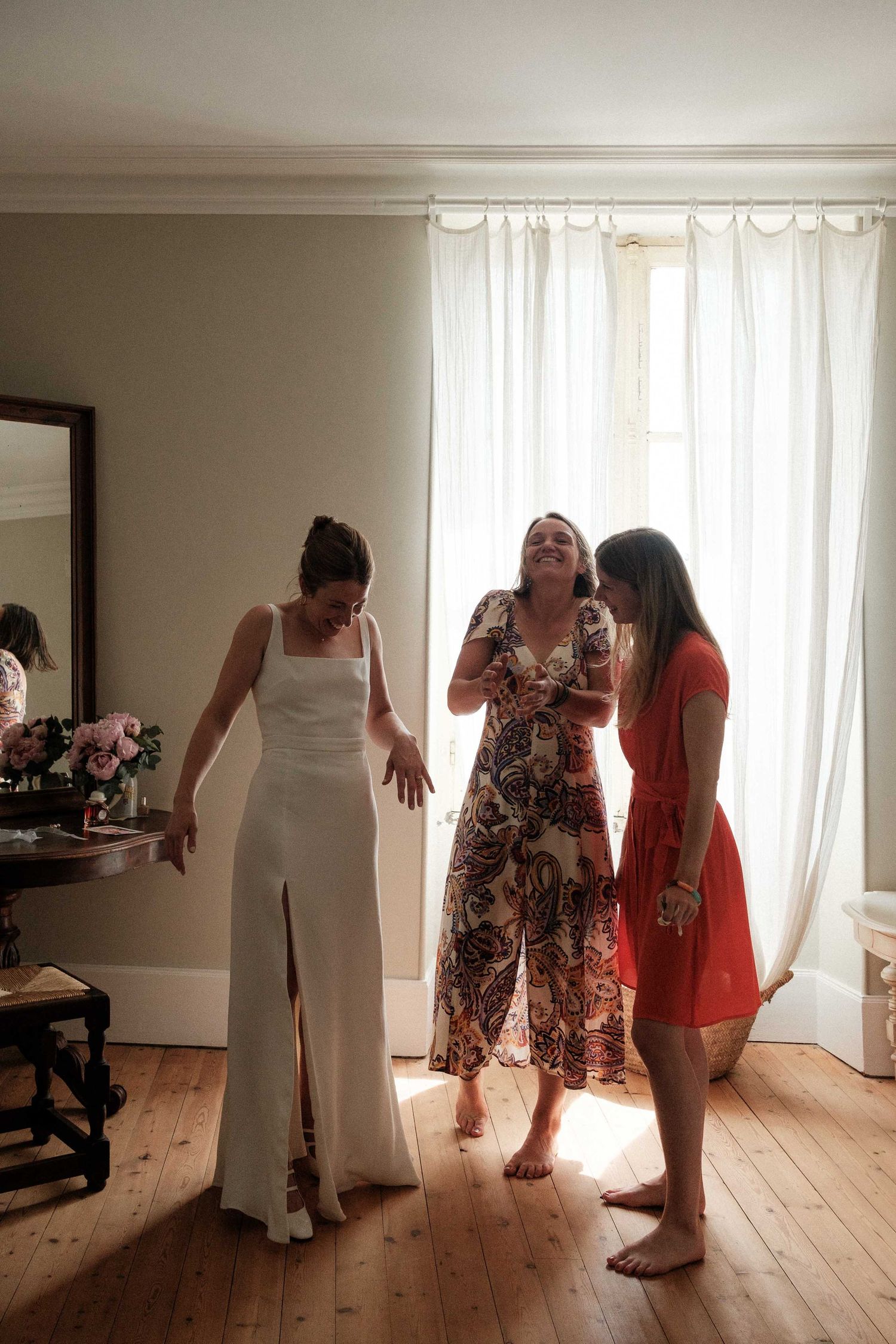 A group of people dancing and laughing together in a bright sunlit room with wooden floors and white curtains.