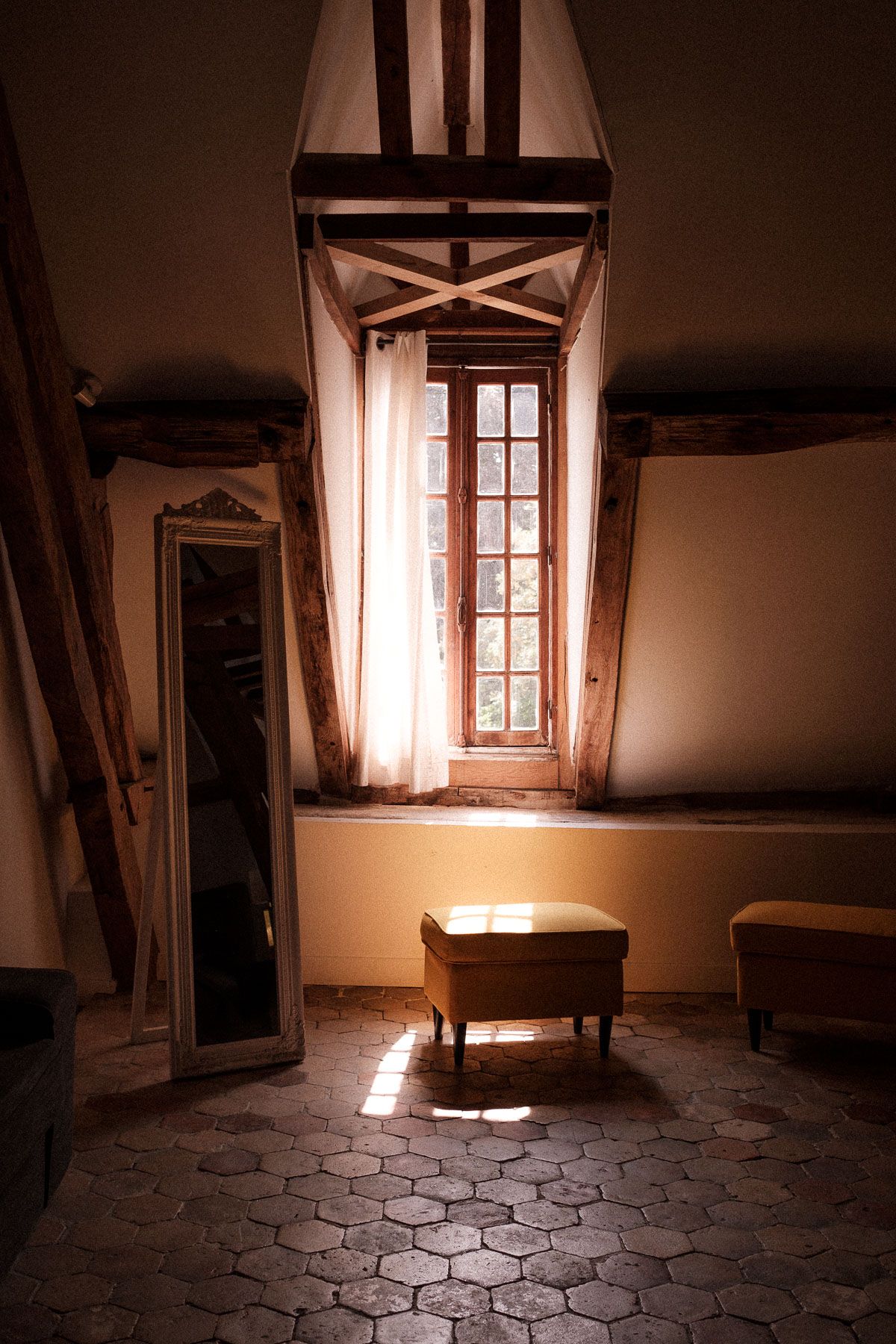 Empty rustic room with hexagonal stone floor tiles and sunlight streaming through a vintage window.