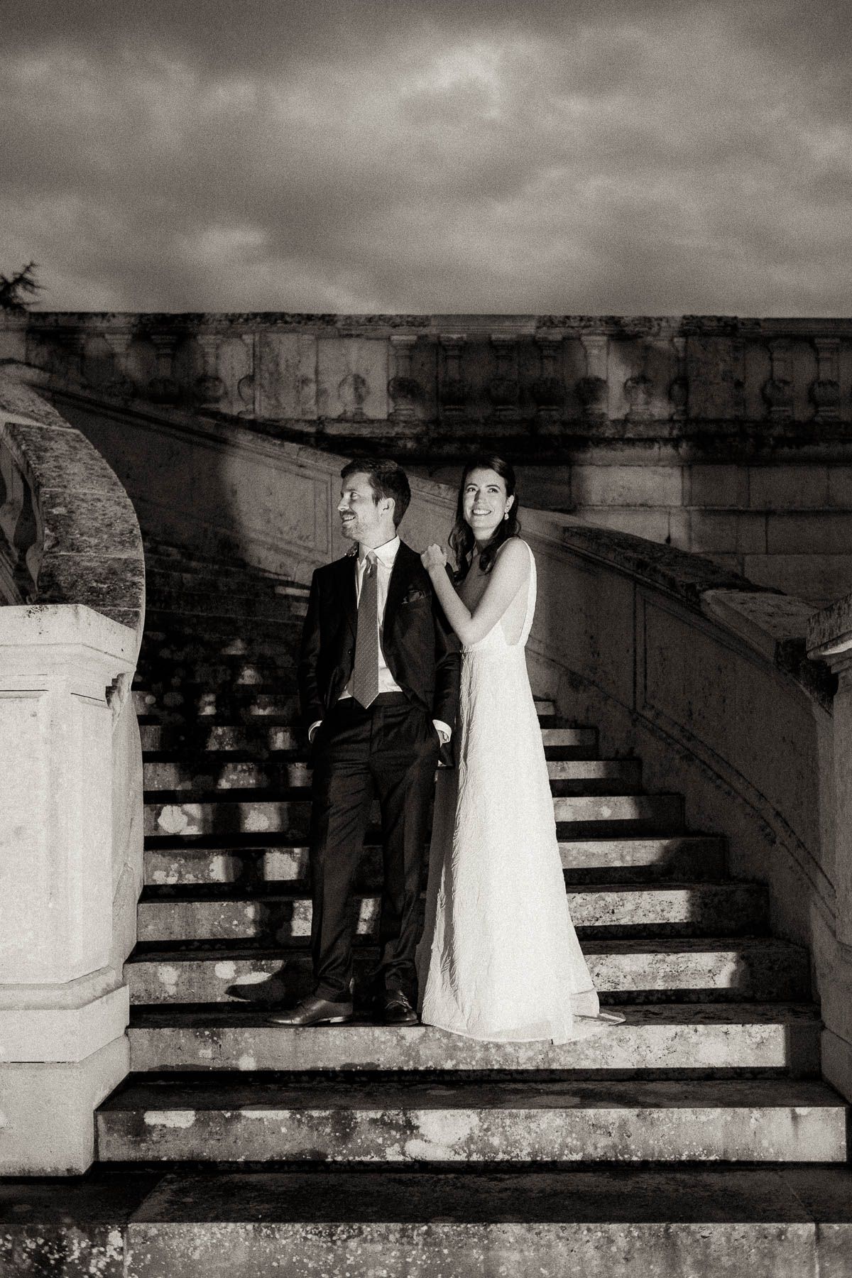 A black and white wedding photo series showing a couple walking down concrete steps in dramatic lighting.