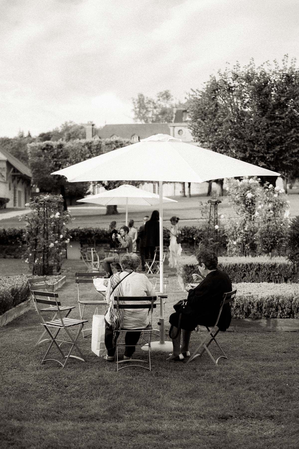 Vintage black and white photo series showing people relaxing under patio umbrellas on a lawn in a residential setting.