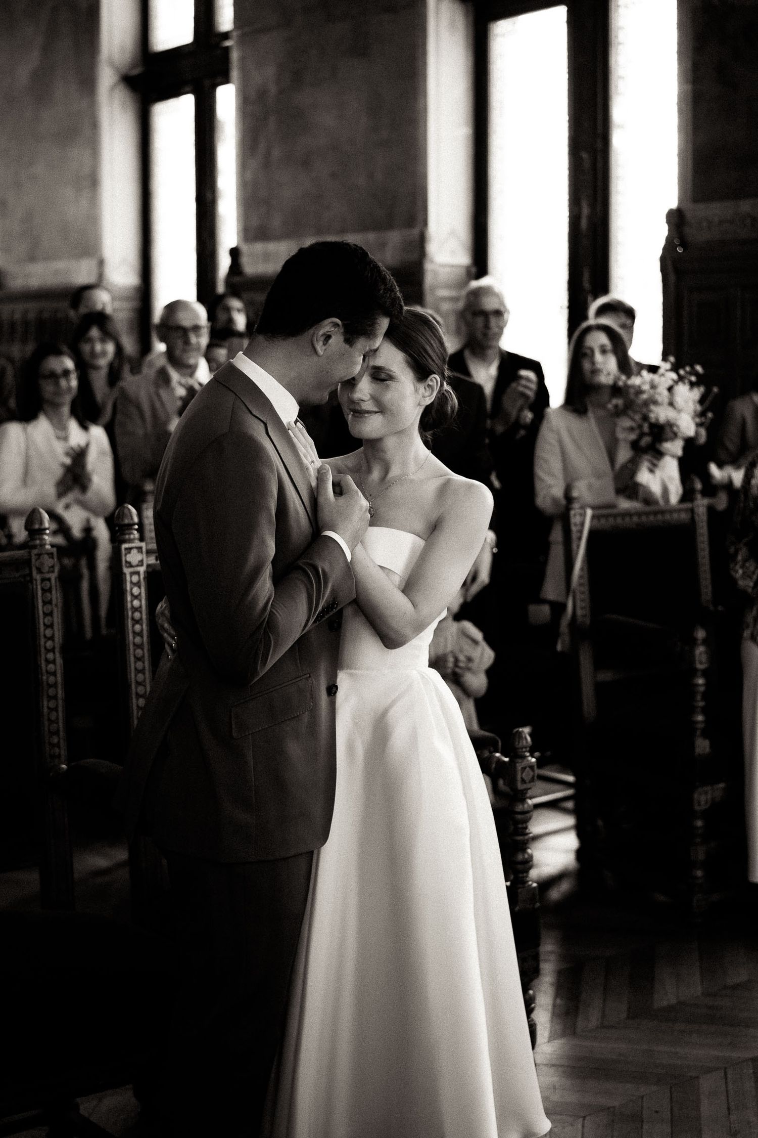 A couple shares their first dance as newlyweds at an elegant indoor reception venue with guests watching in the background.