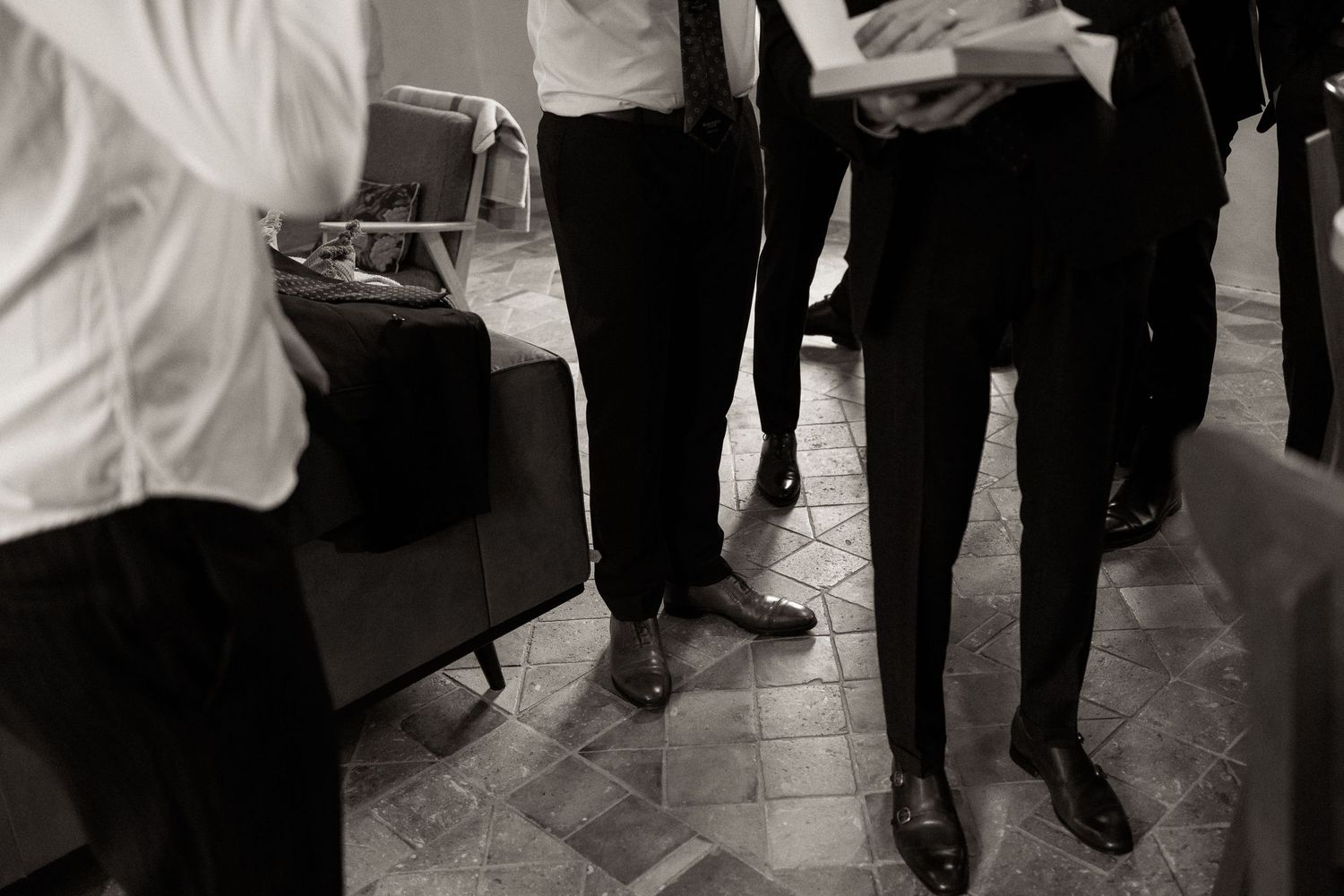 A group of people in formal attire walk across a dark floor with white lighting and reflections.