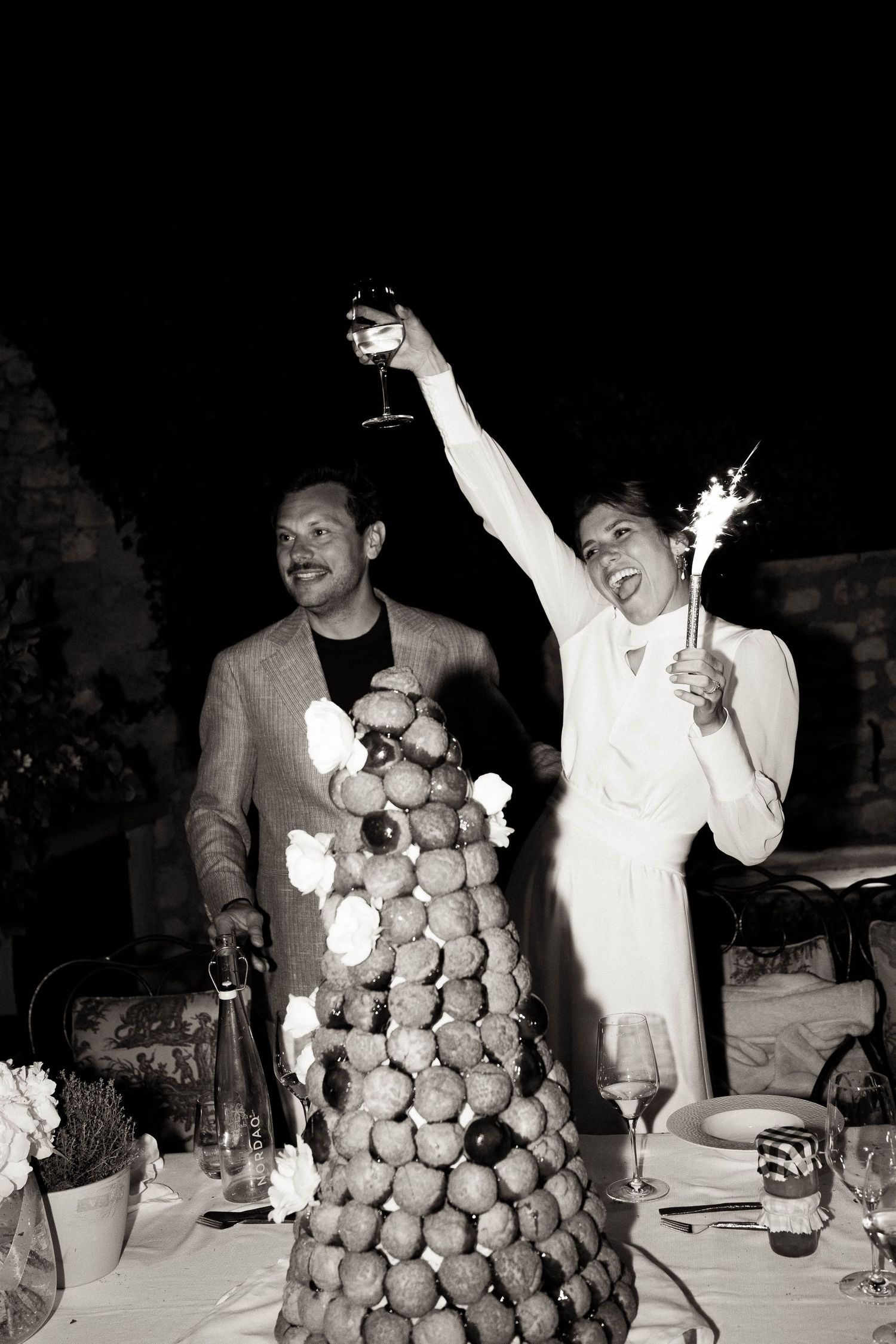 A black and white photo of a wedding celebration with a croquembouche dessert tower and champagne toast.