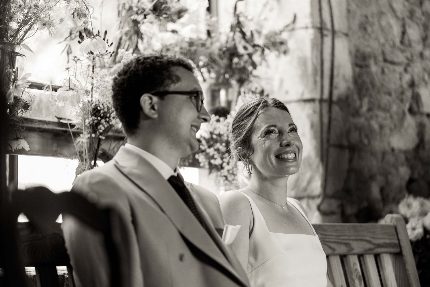 A black and white candid moment of a couple sharing laughter during their wedding ceremony.