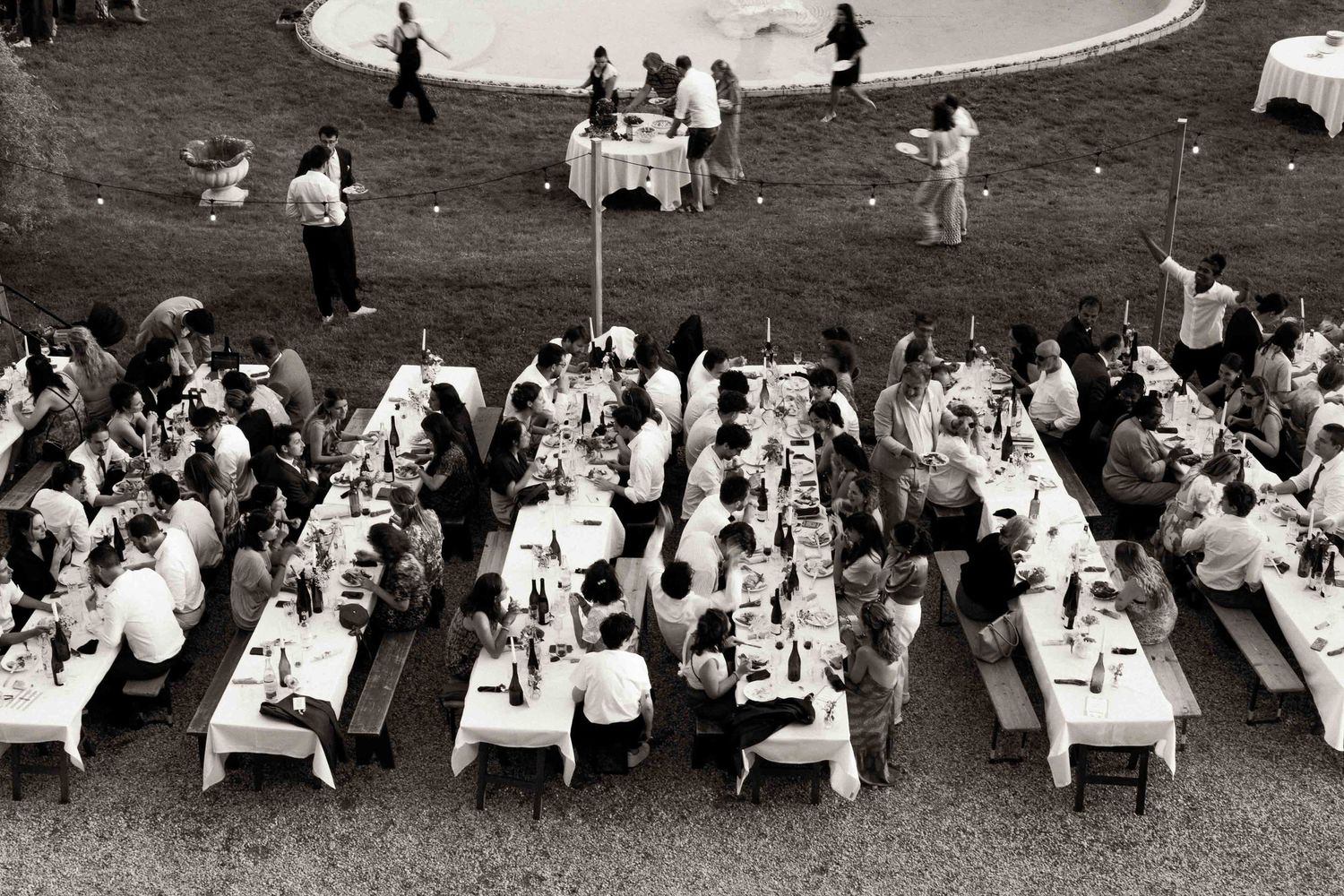 Aerial black and white view of people gathered at multiple long banquet tables for an outdoor celebration.