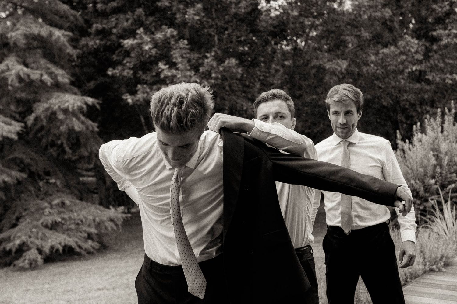 Groomsmen in white shirts helping each other get dressed before a wedding ceremony.