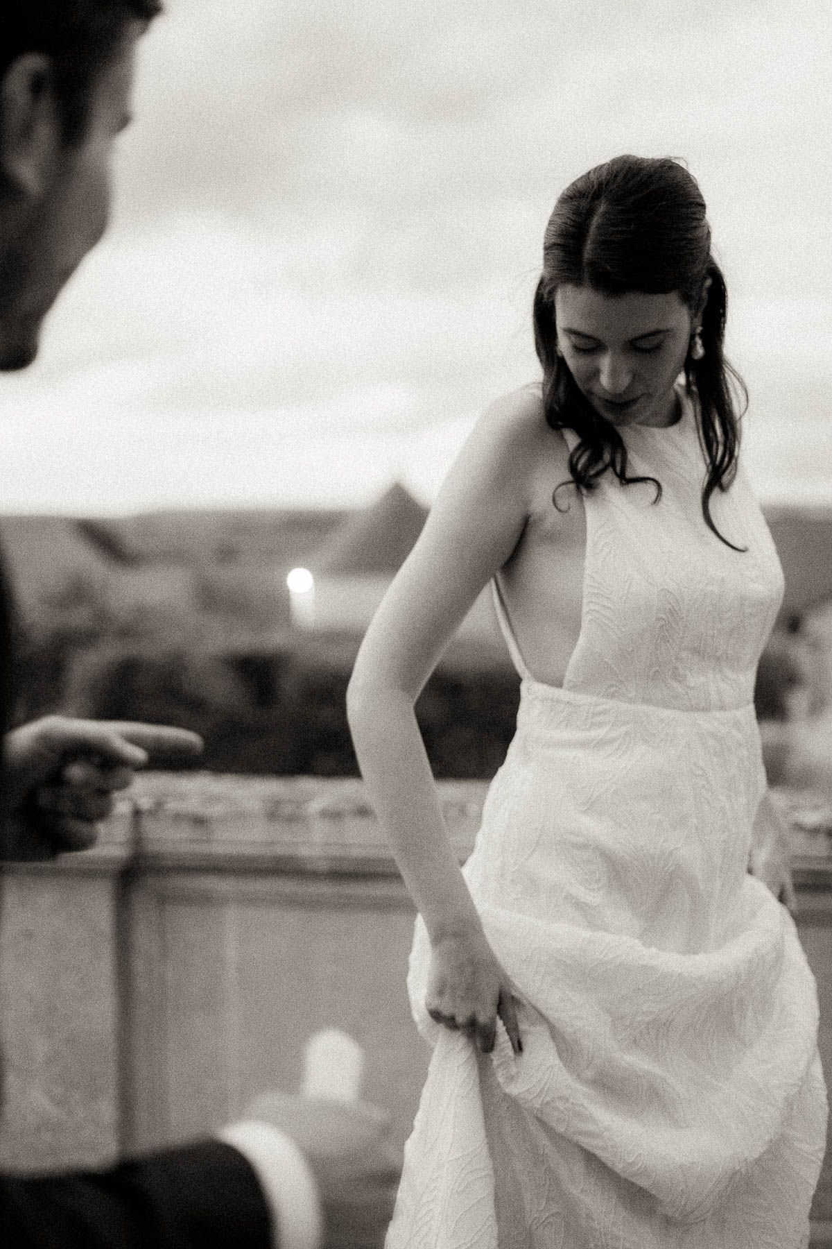 A candid black and white wedding photograph showing a bride in a strapless white dress smiling and looking down.
