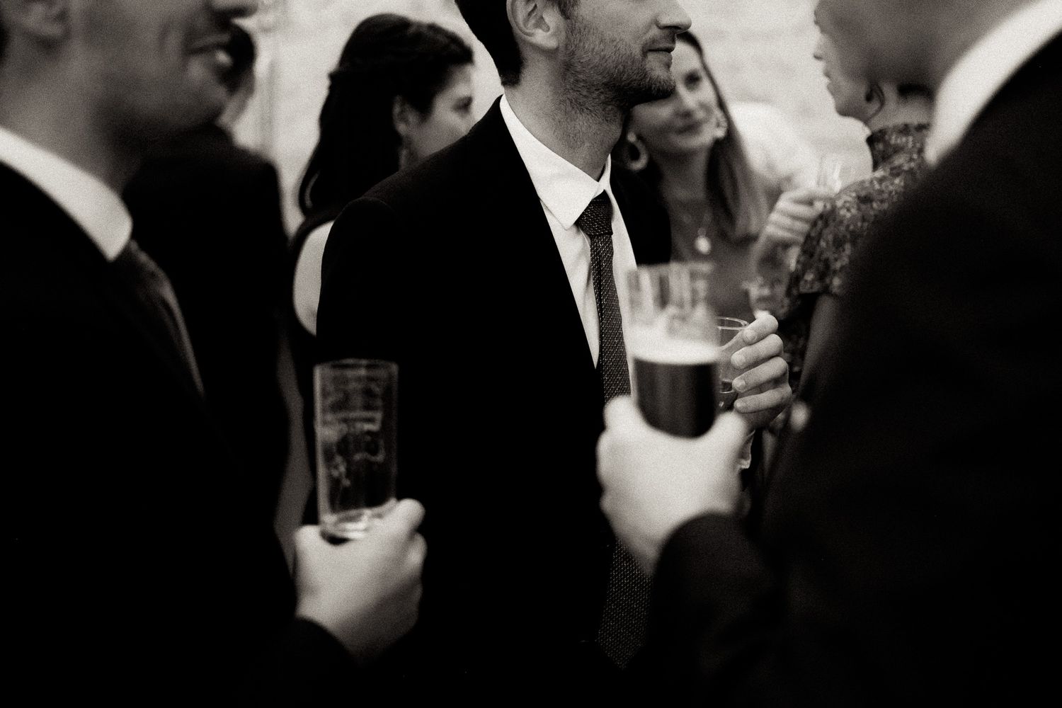 A person wearing a black suit and tie holds a microphone while speaking at a formal event.