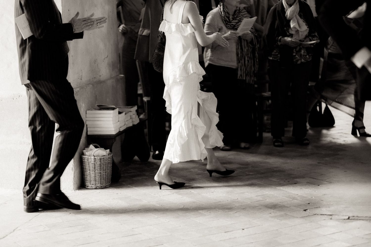 Black and white photograph of wedding guests dancing and mingling at a reception with a woman in a flowing white dress.