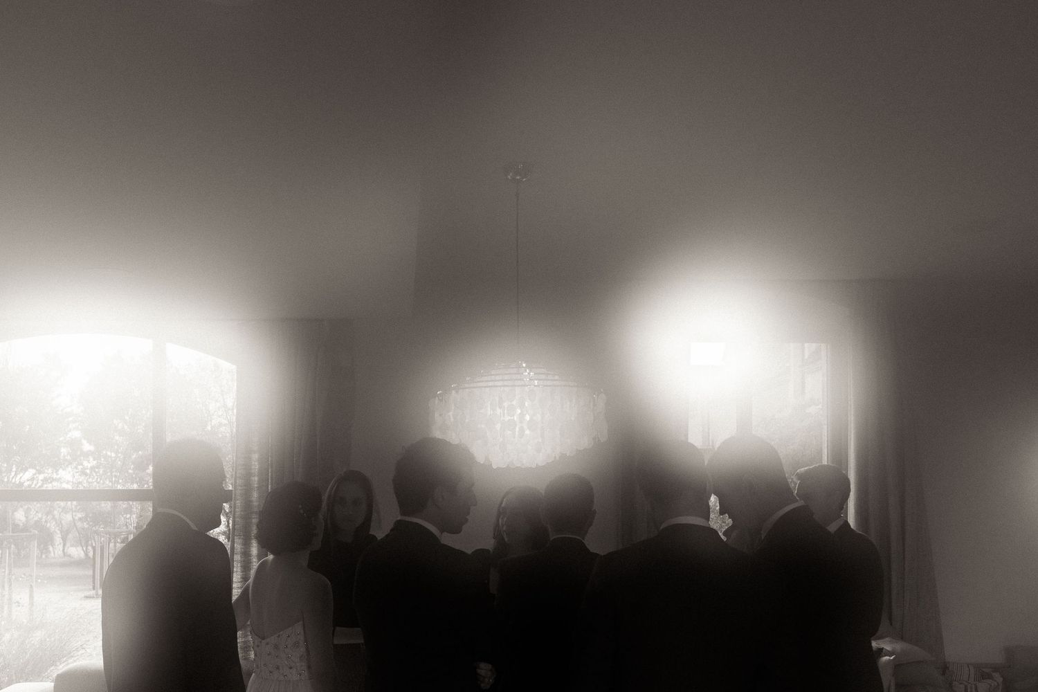 A dark concert venue with silhouettes of performers on stage illuminated by bright spotlights and hazy atmosphere.