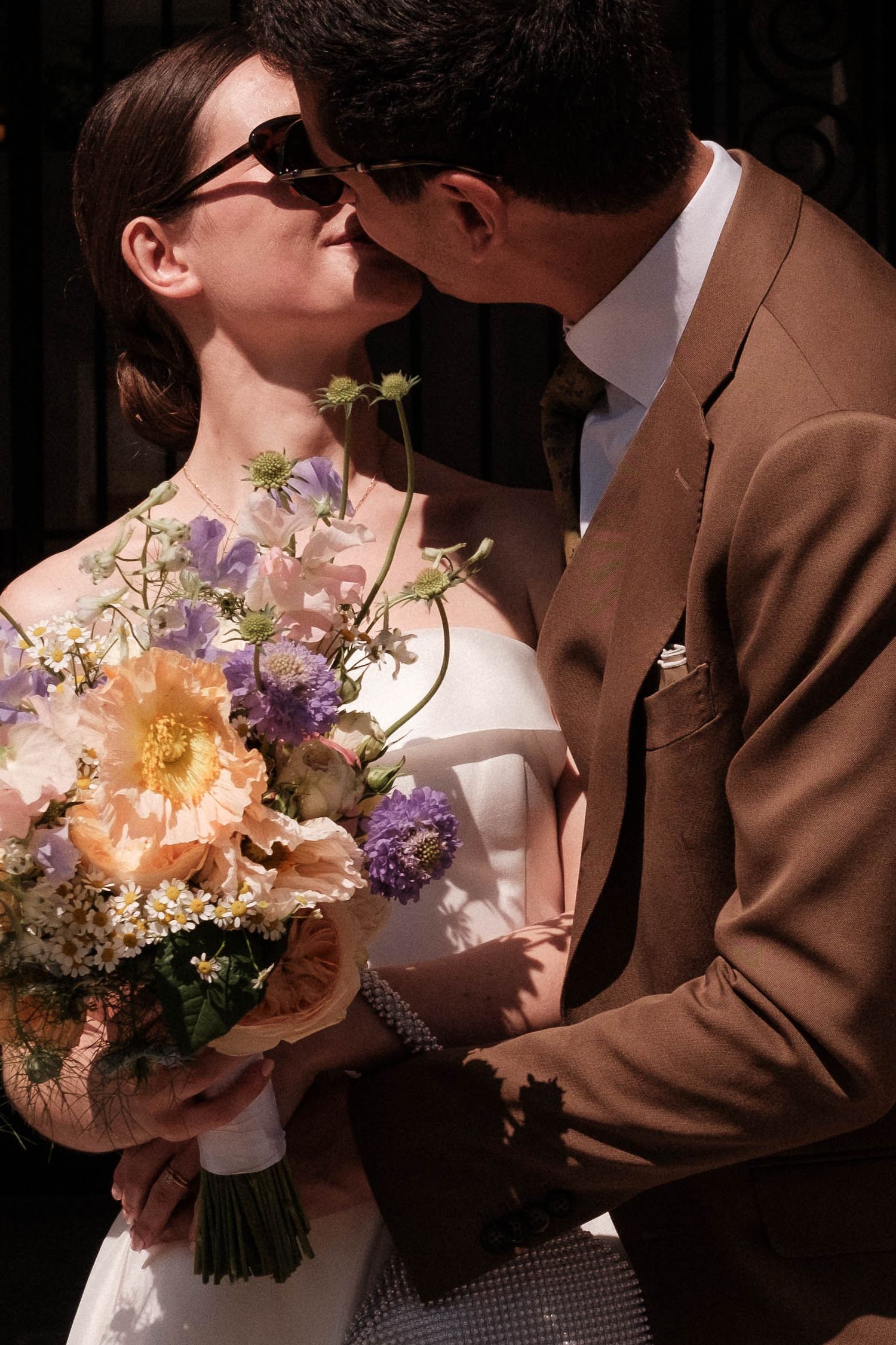 A romantic couple in brown and white share intimate moments while holding a bouquet of peach and purple flowers.