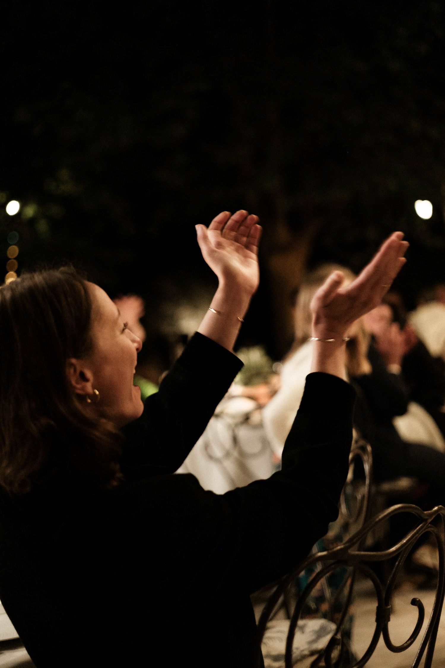 A person in black raises their hands in worship during an evening church service or concert.