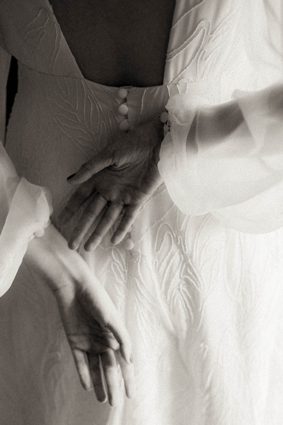 Black and white artistic photograph showing hands delicately touching white fabric in a minimalist composition.